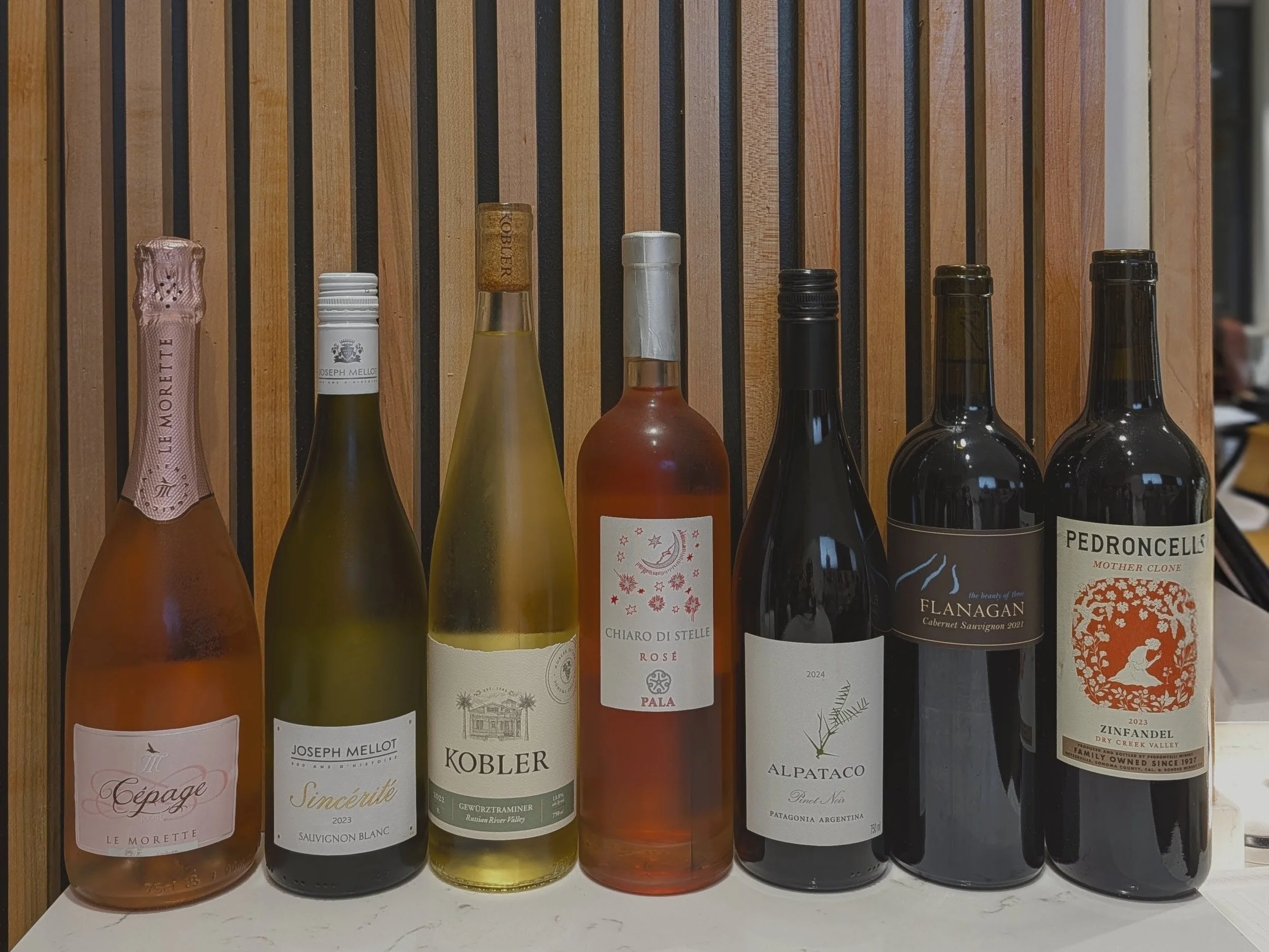 seven wine bottles sit in a row on a counter showing the labels