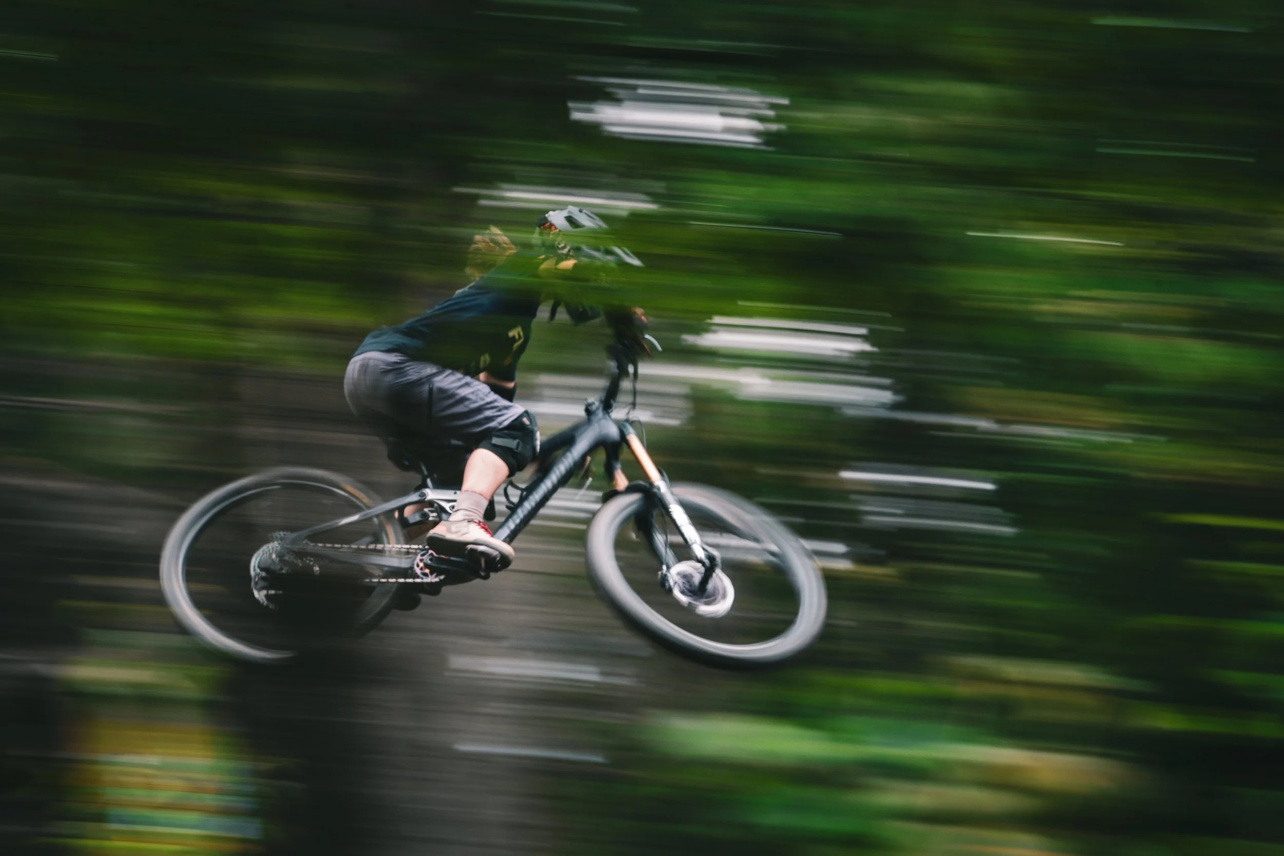 A person mountain biking through a blurred forest trail while wearing a helmet and sports gear.