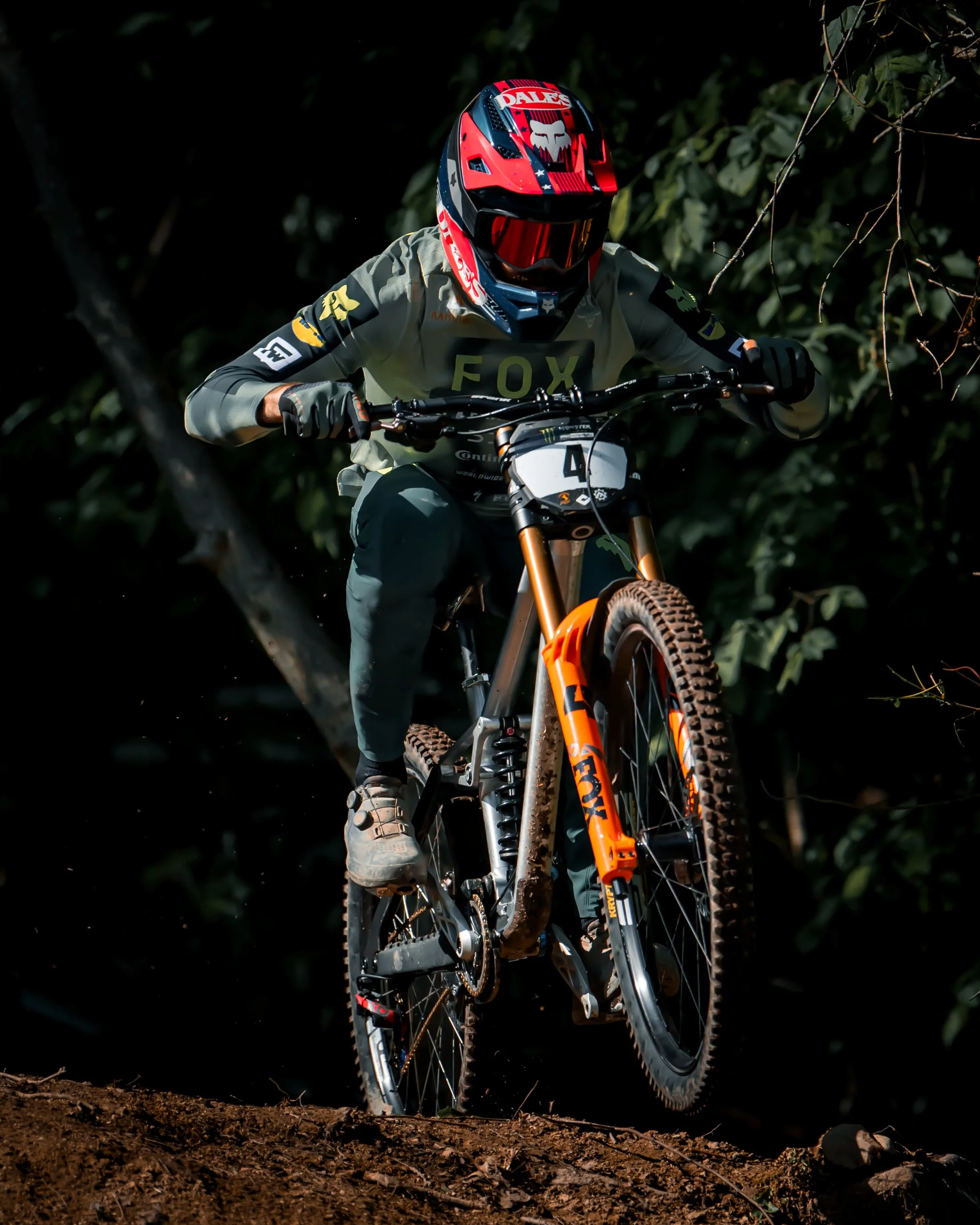 A mountain biker wearing a helmet and riding gear, navigating a dirt trail with trees in the background.