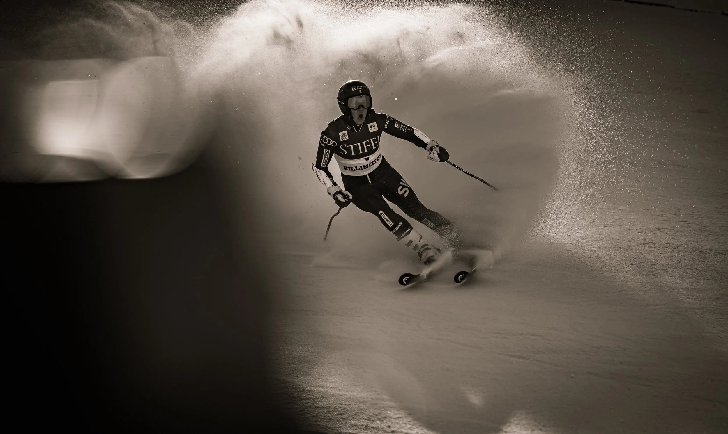 A skier in racing gear navigating a turn on a snowy slope, surrounded by snow spray.