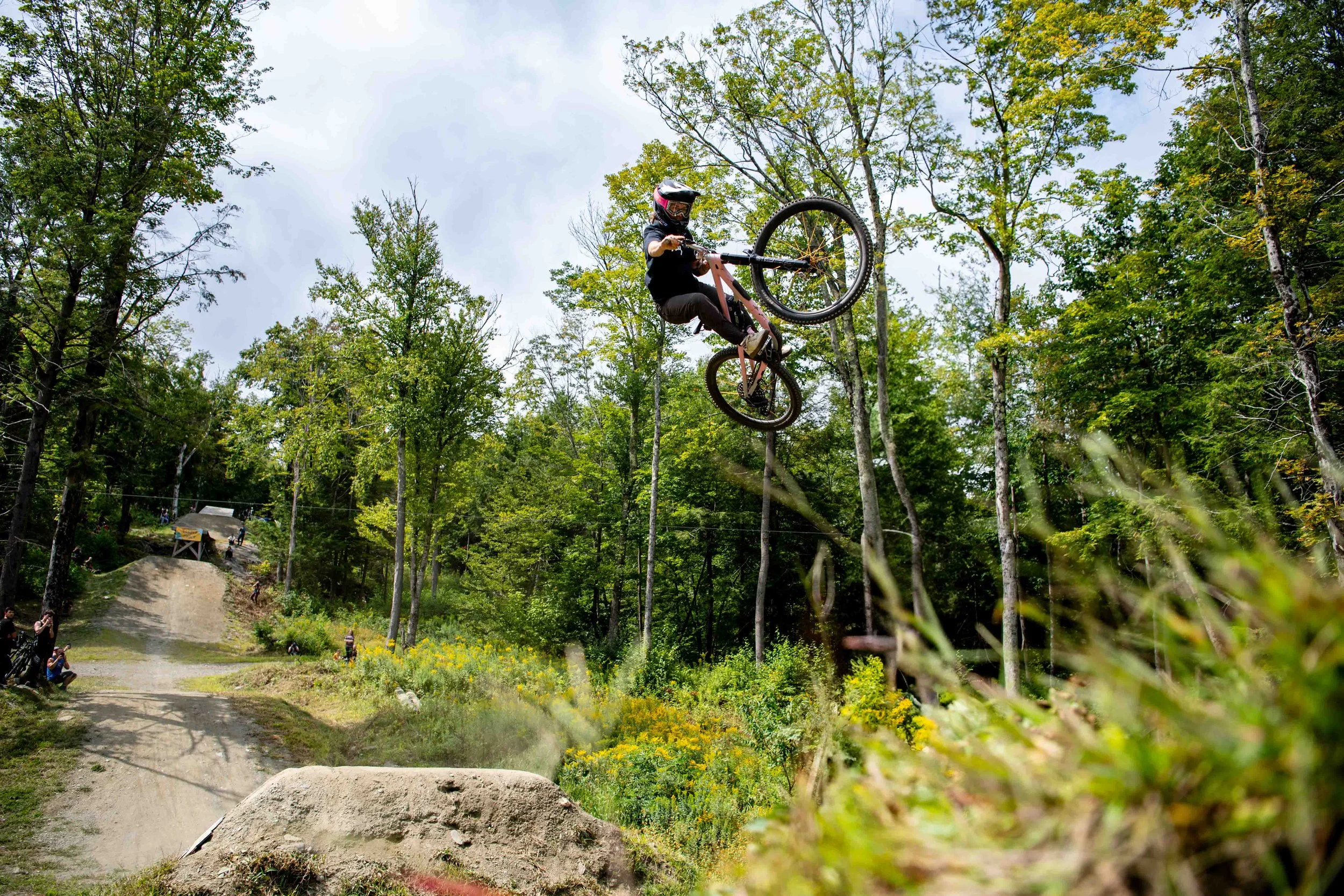 A person performing a jump on a mountain bike in a wooded area during a mountain biking event.