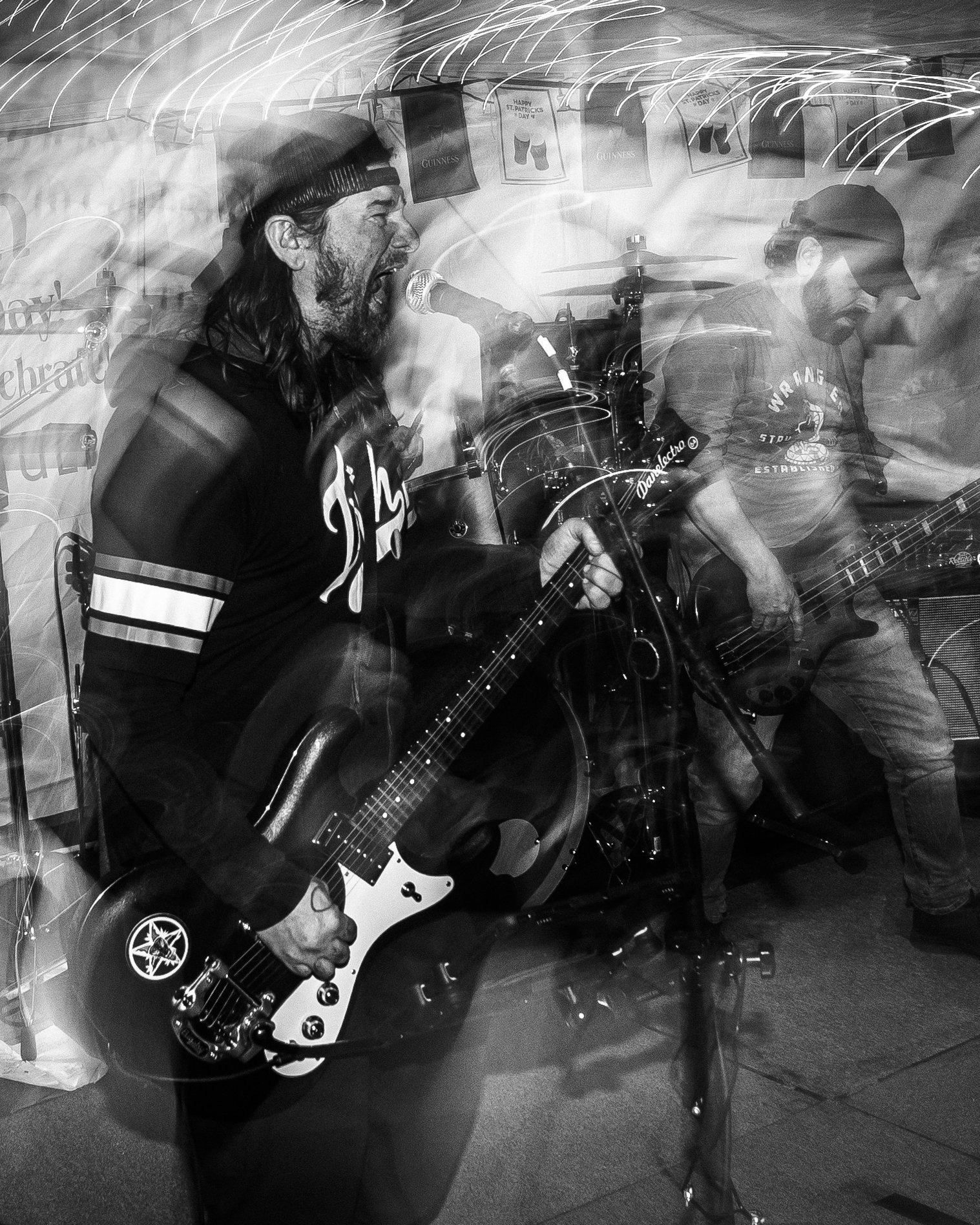 Black and white photo of two musicians playing guitars and singing into a microphone during a live performance in a small venue.