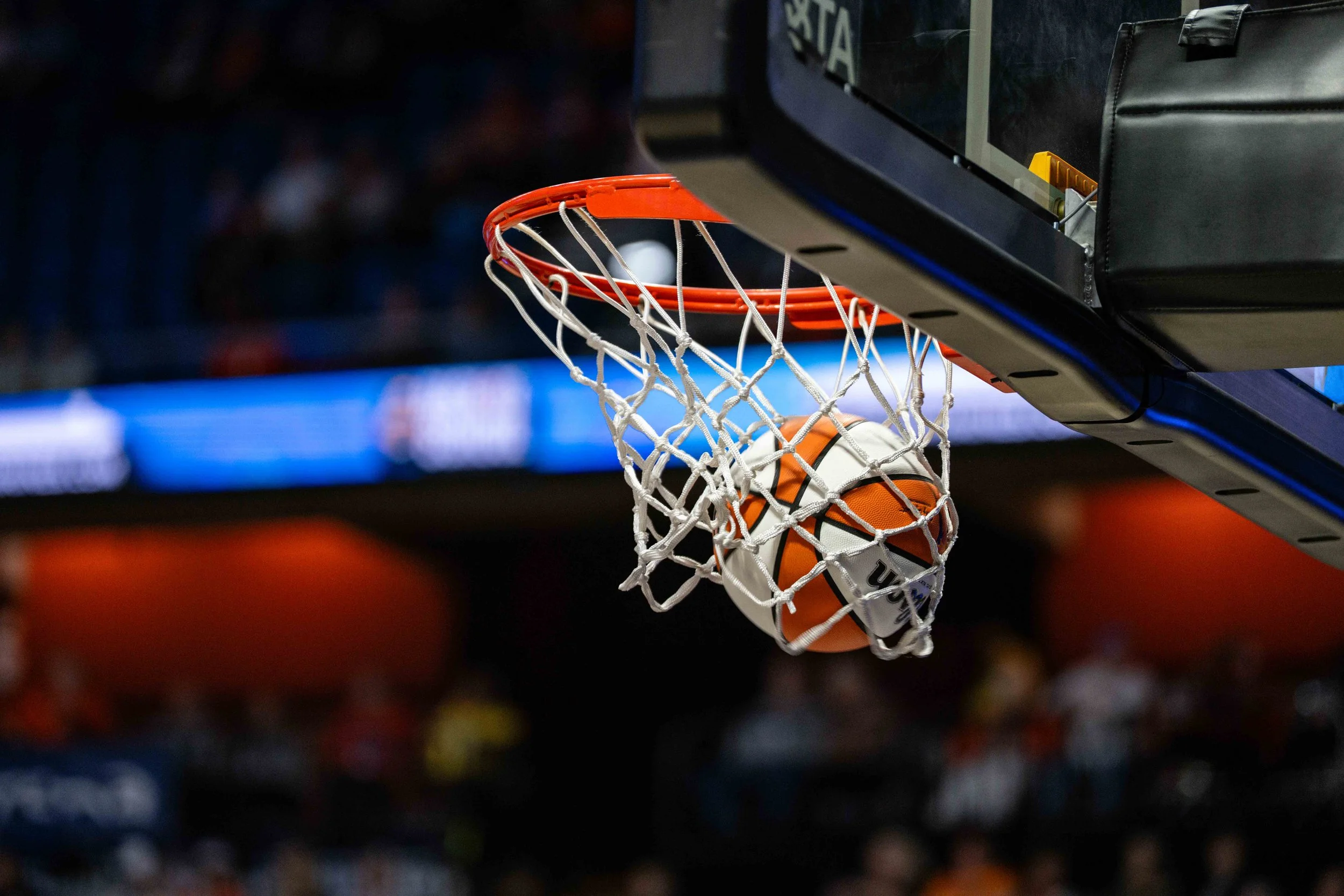 A basketball going through a hoop in an indoor basketball arena.