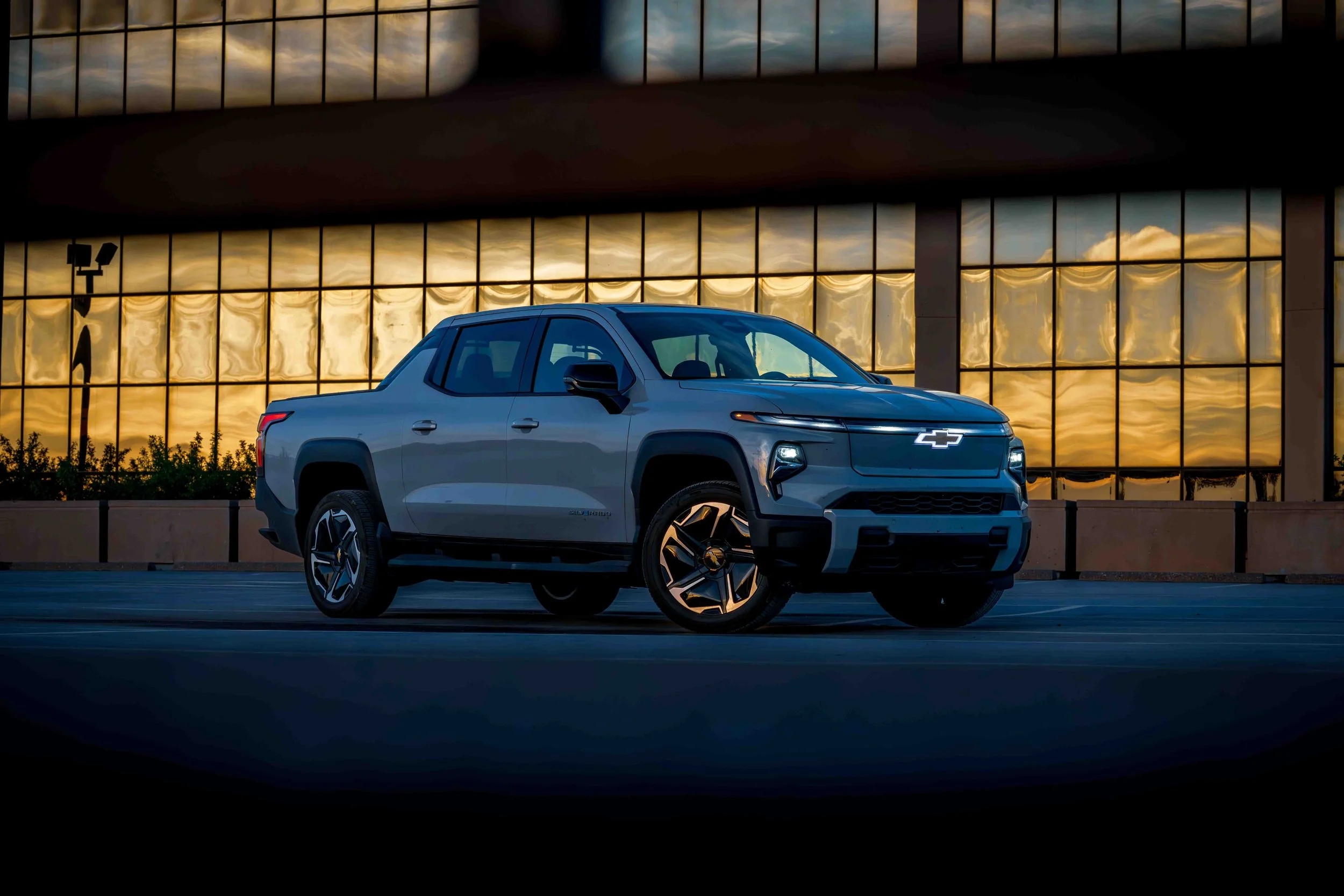 A gray Chevrolet pickup truck parked outdoors during sunset, with a reflective building in the background.