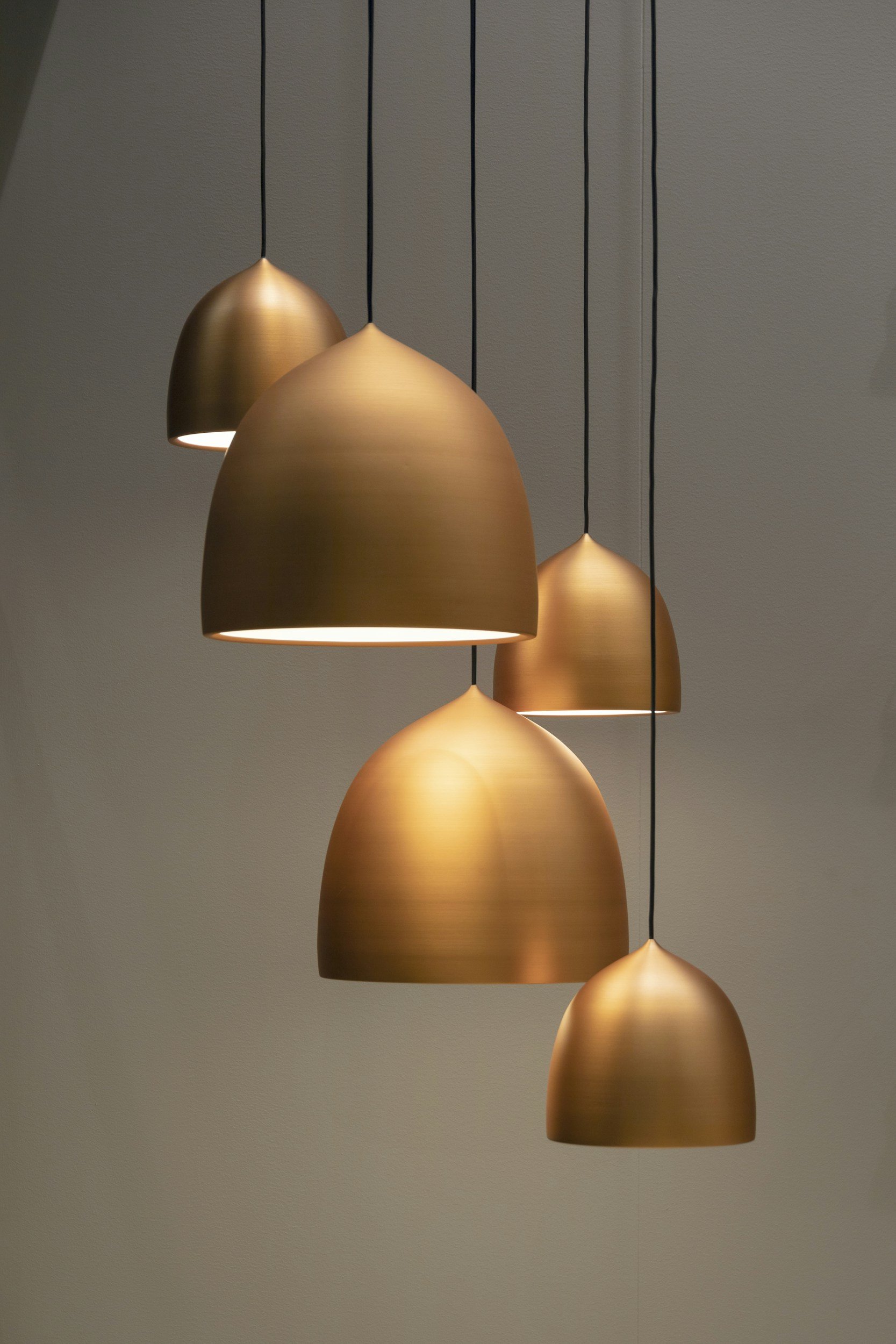 Five gold pendant lights hanging from black cords against a plain wall.