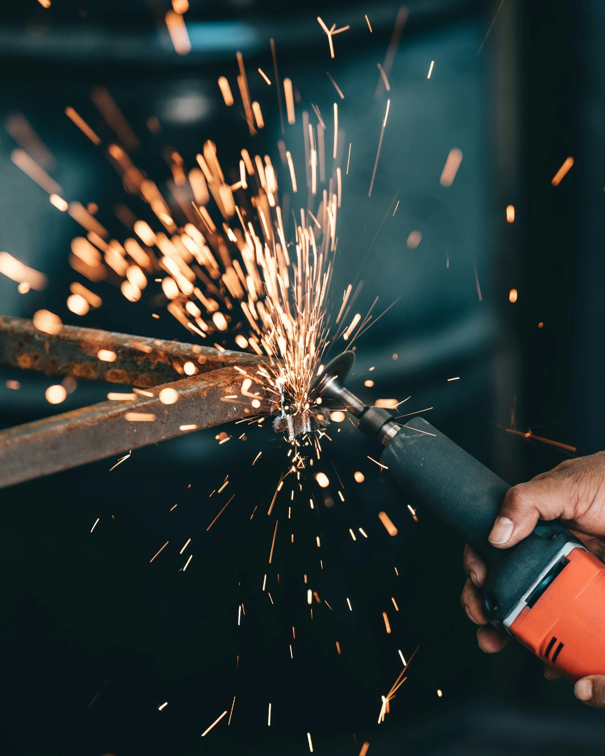 A person using a power tool to cut or grind a piece of metal, producing sparks.
