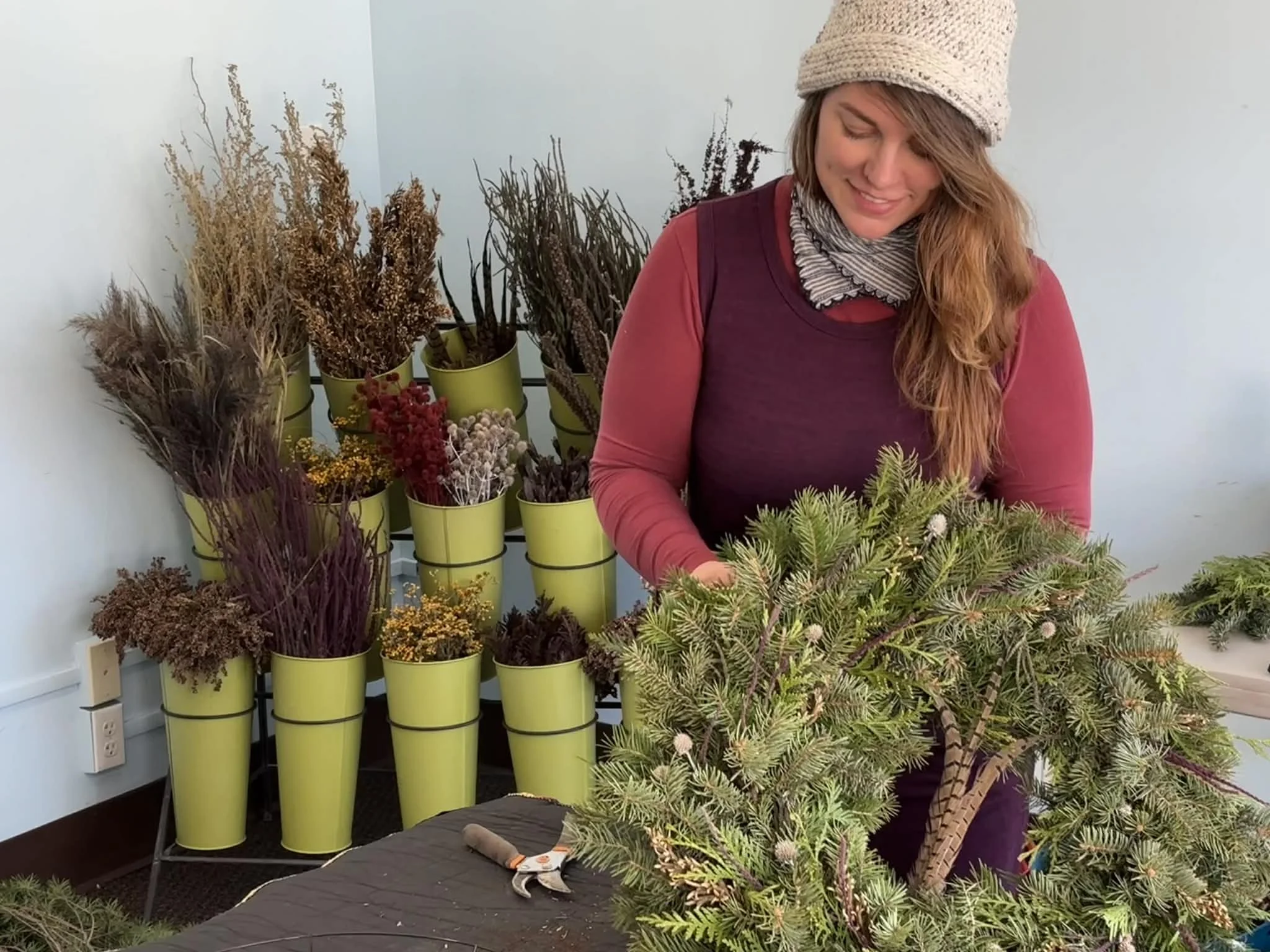 Good Services offering wedding and event florals in Des Moines Iowa owner Lindsey Good arranging a small pine tree with display of dried flowers in green pots.