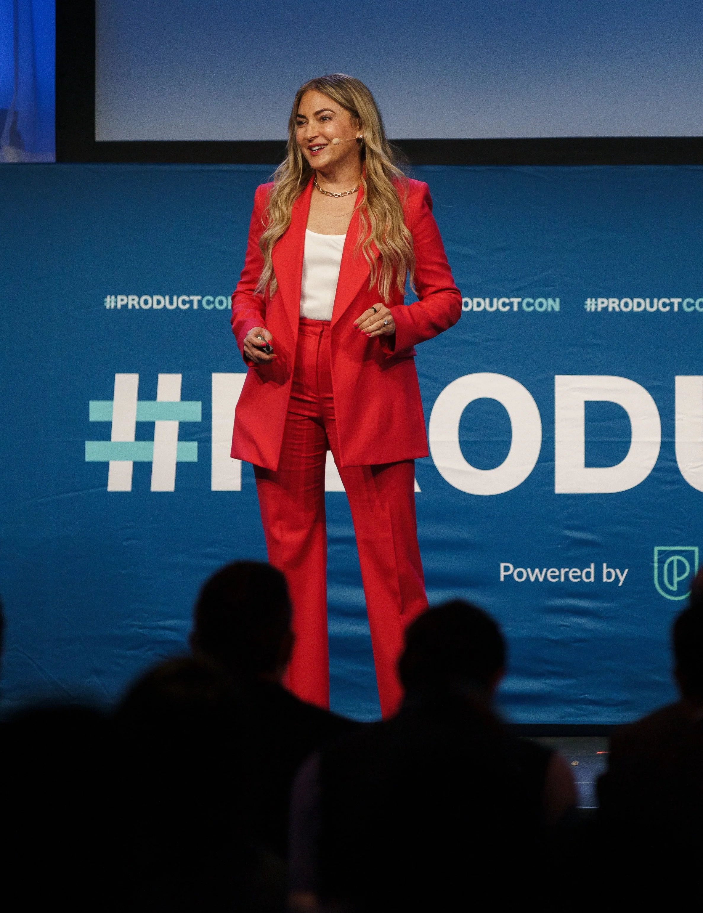 A woman in a red suit giving a presentation at a conference.