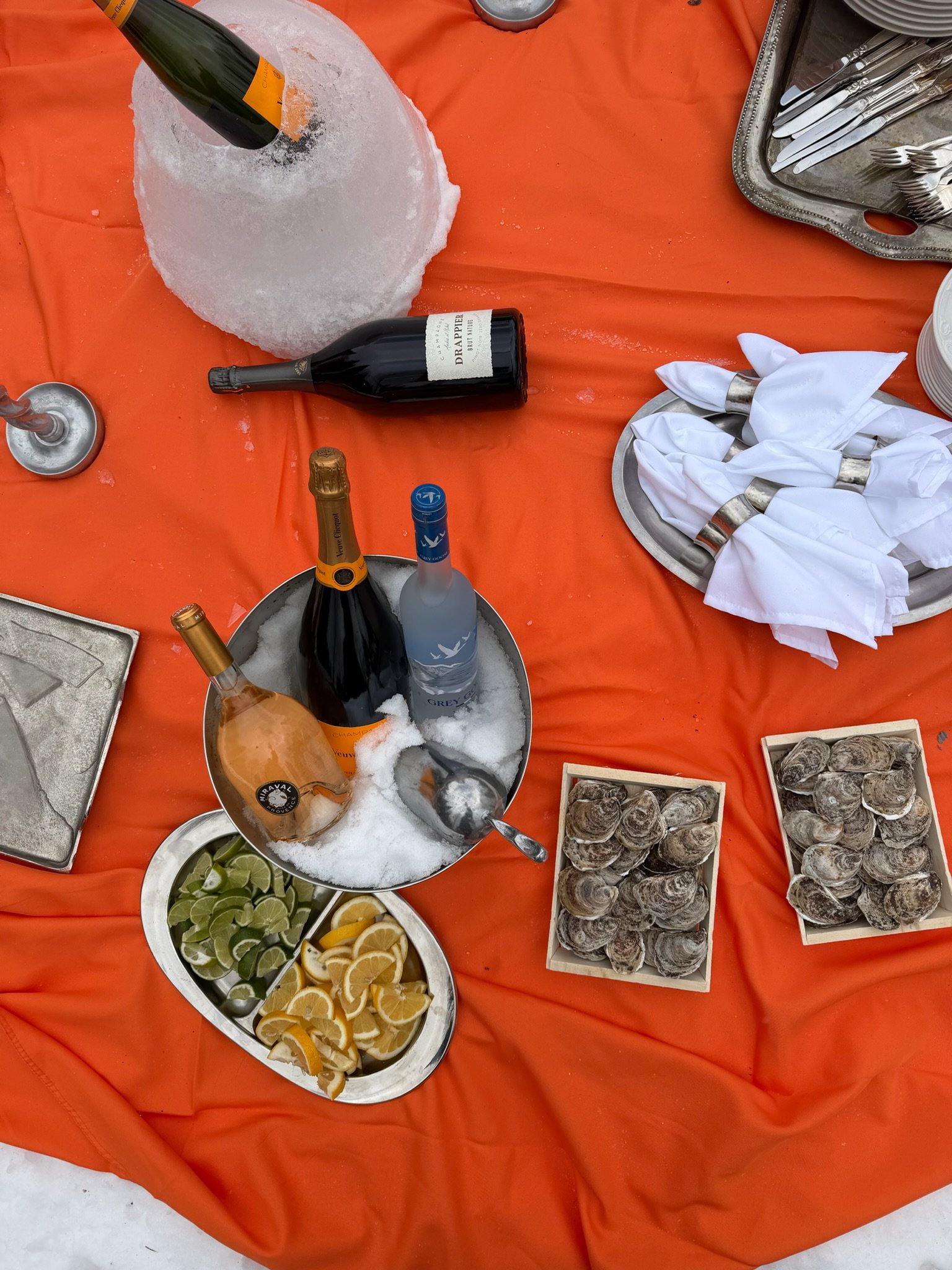 Table dressée avec des fruits, des boissons, des coquillages et des couverts, pour un repas ou un événement en plein air.