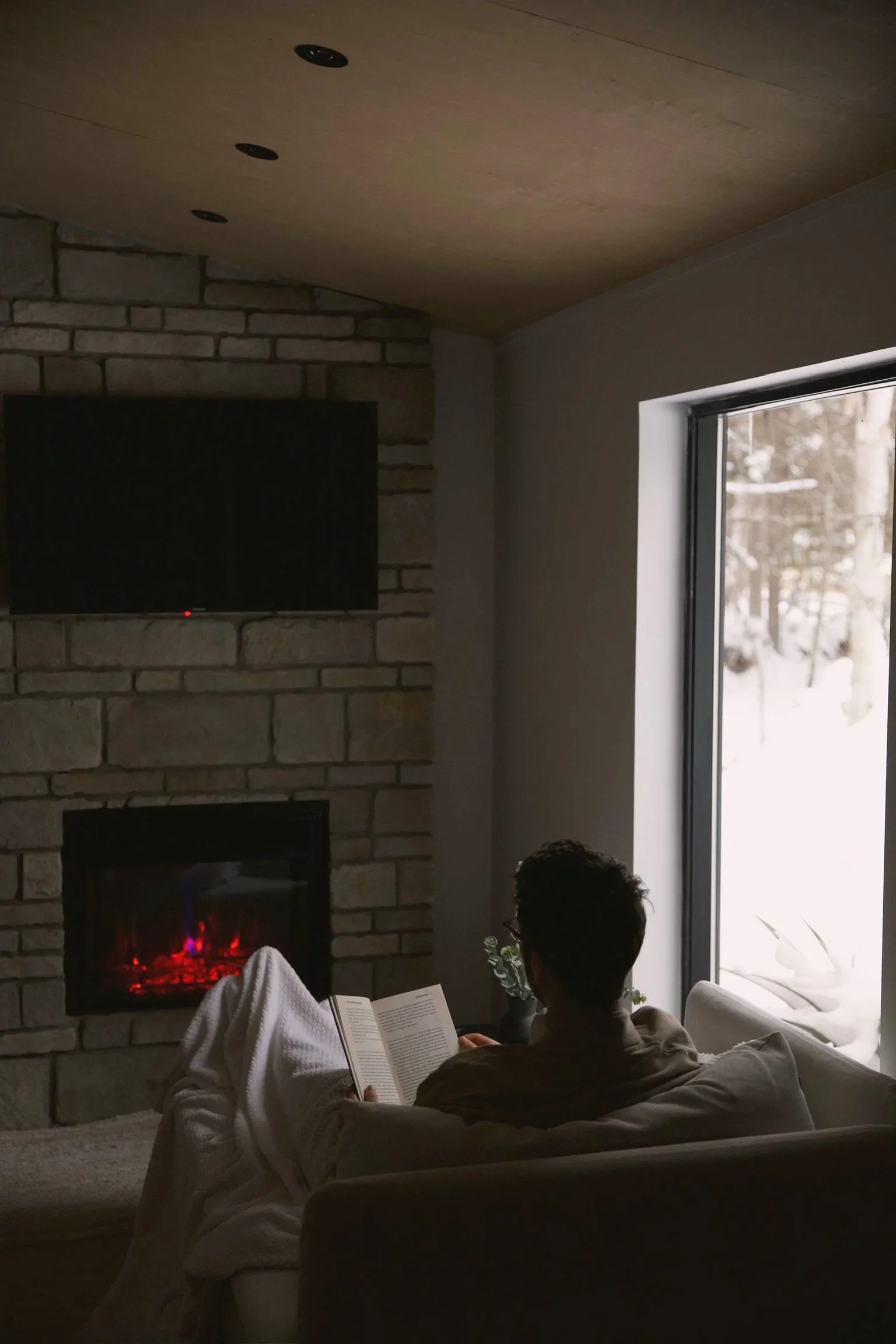 Lecture au coin du foyer dans une chambre, vue sur la forêt enneigée