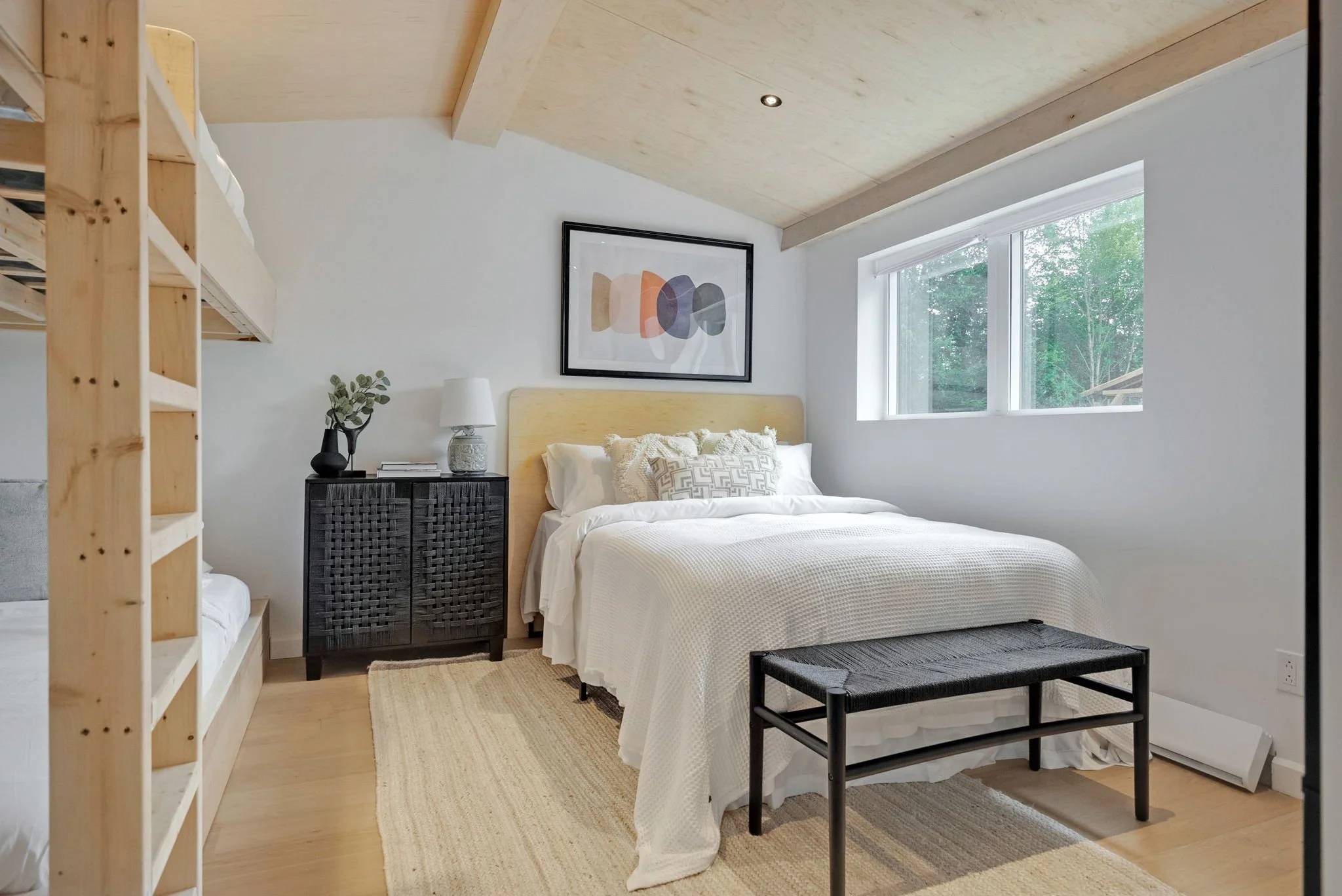 Chambre moderne avec lit blanc, tête de lit en bois, tableau abstrait, grande fenêtre laissant entrer la lumière naturelle, meuble noir, tapis beige, banquette noire, mobilier minimaliste, murs blancs, plafond en bois clair.
