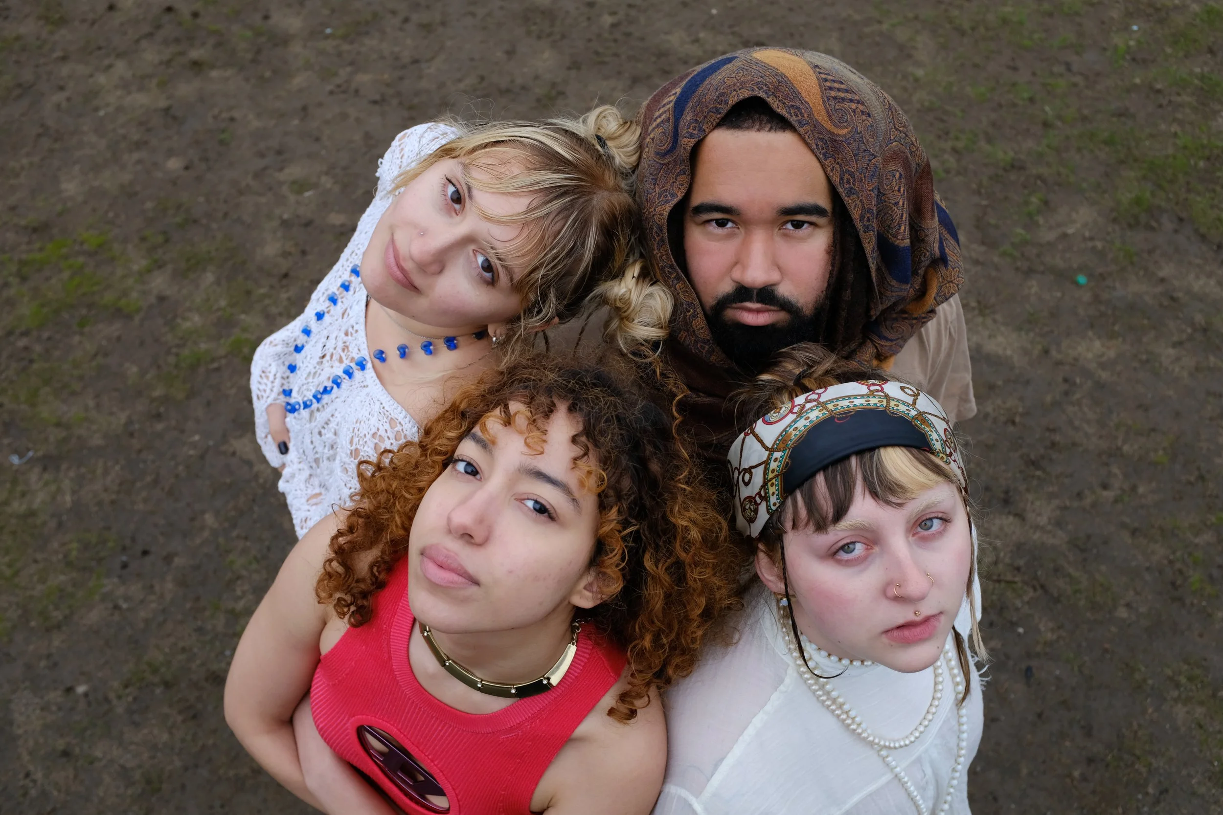 A diverse group of five young women looking up at the camera, with a dirt ground background.