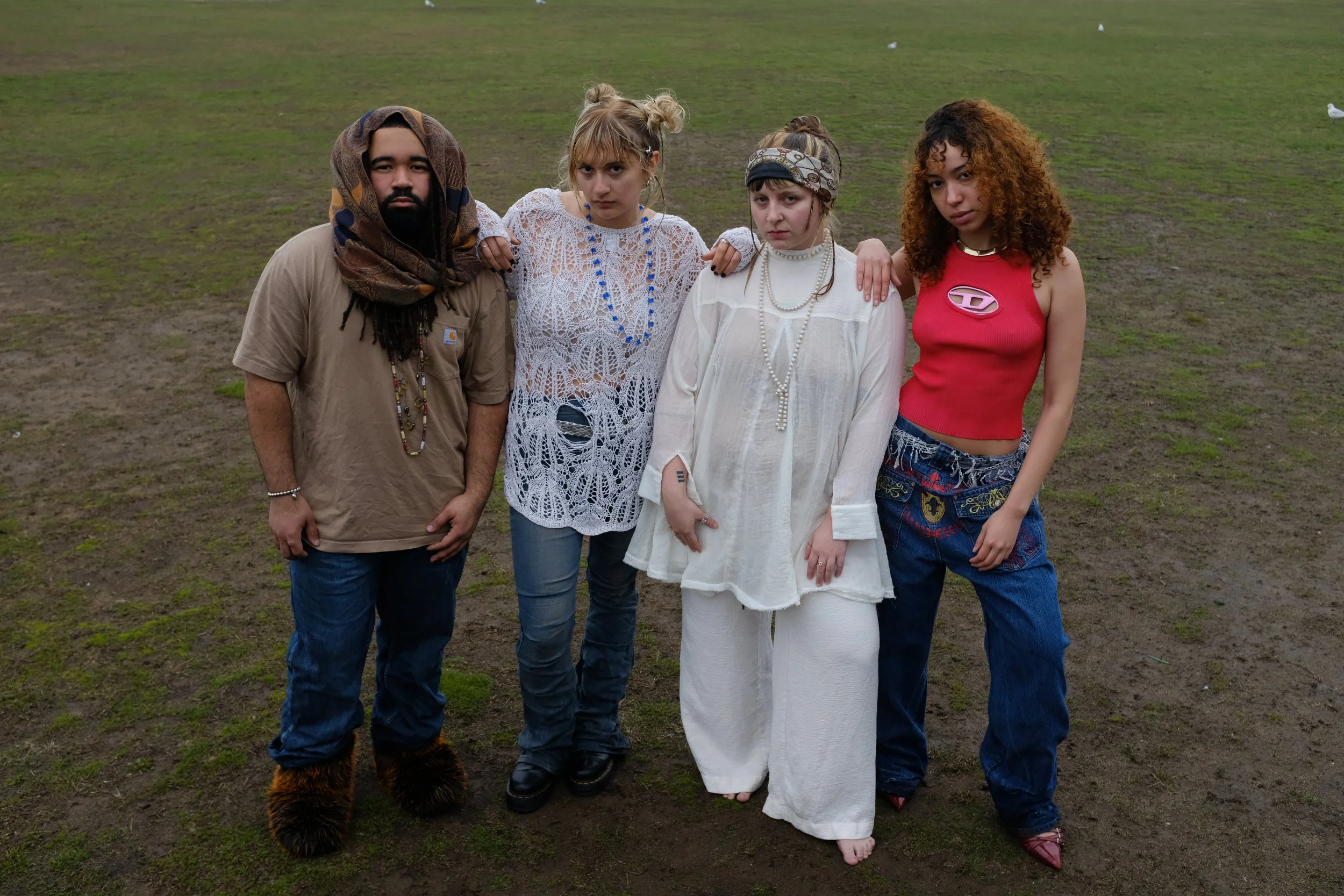 Four young adults standing on a grassy field, posing closely together for a photo.