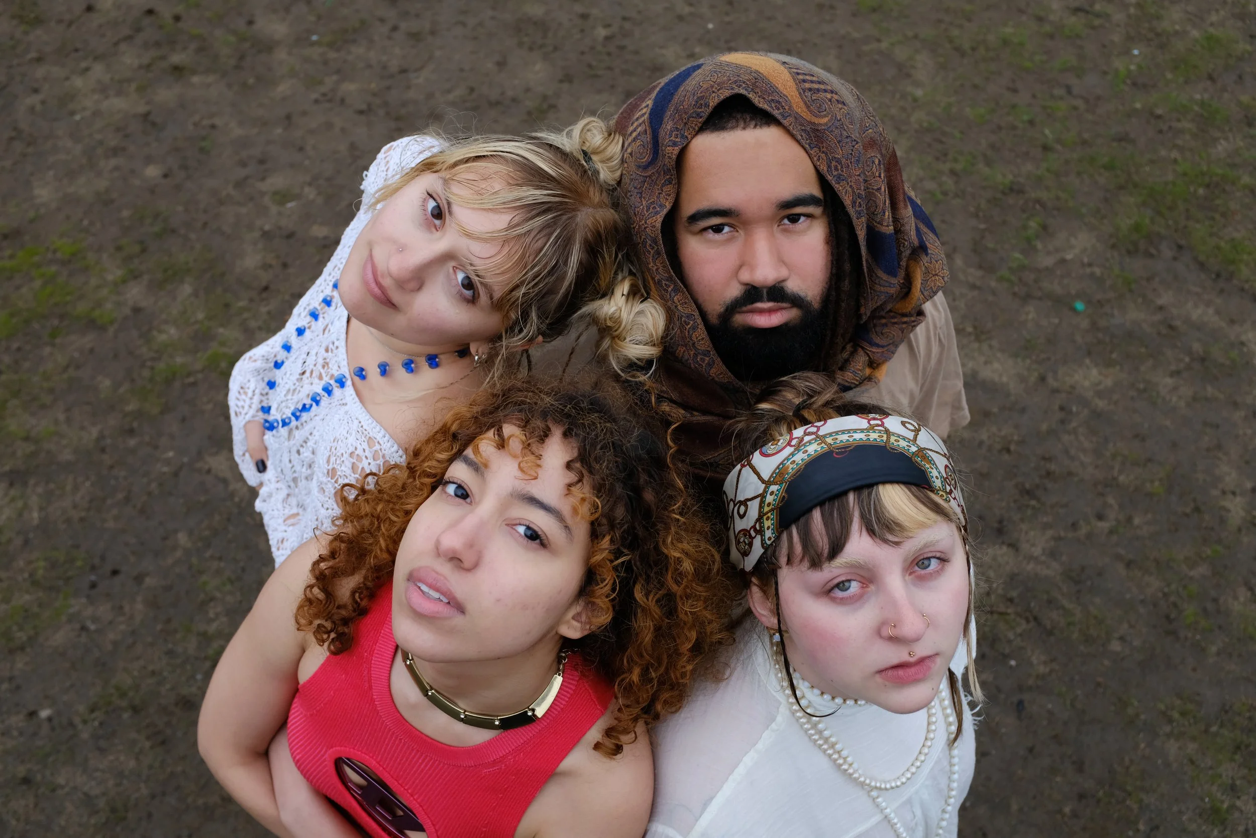 A group of five young adults standing closely together outside, looking directly at the camera, with a muddy ground background.