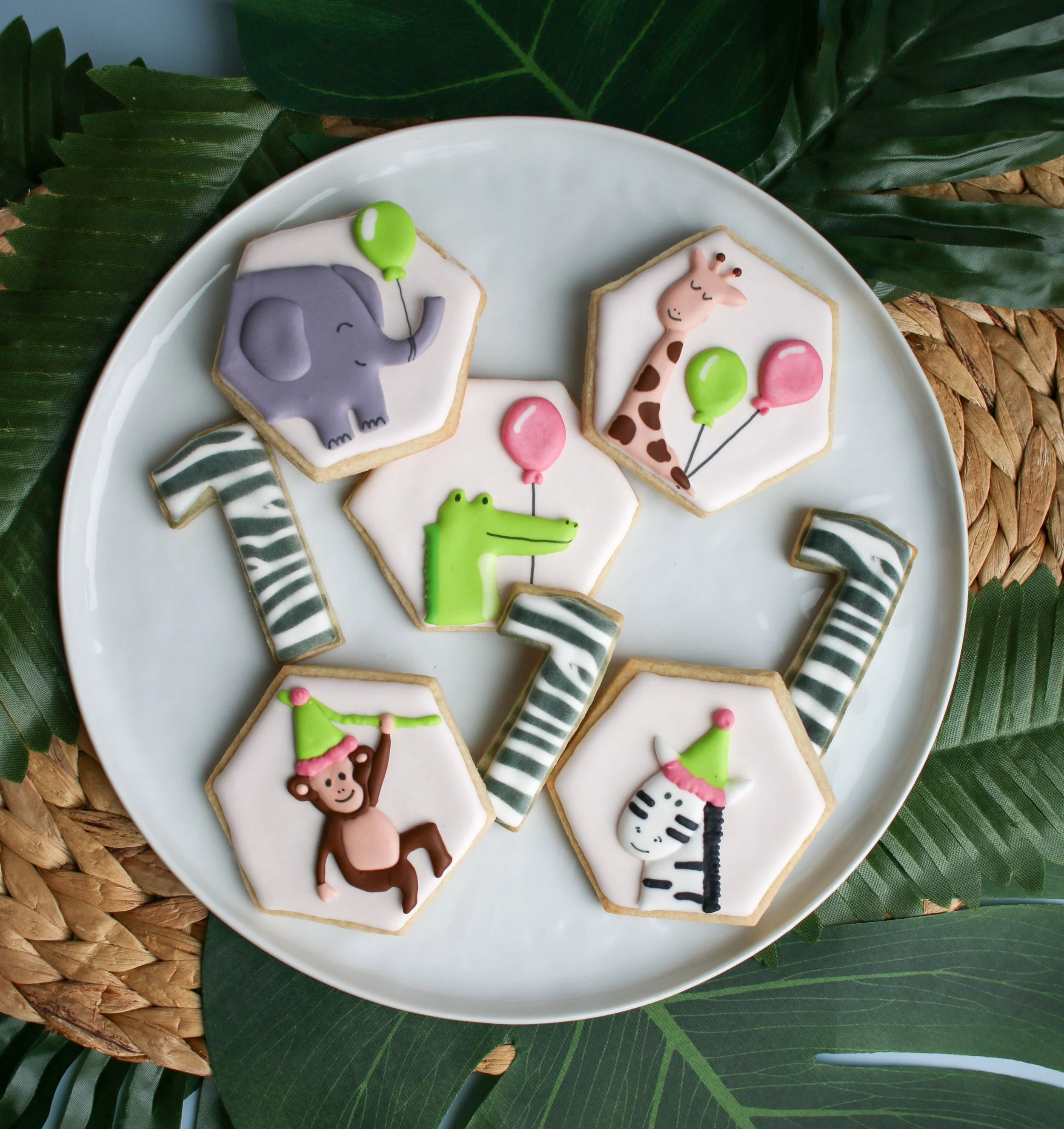 Plate of decorated cookies with jungle animal designs and number 1 decorations, on a plate with green leaves background.