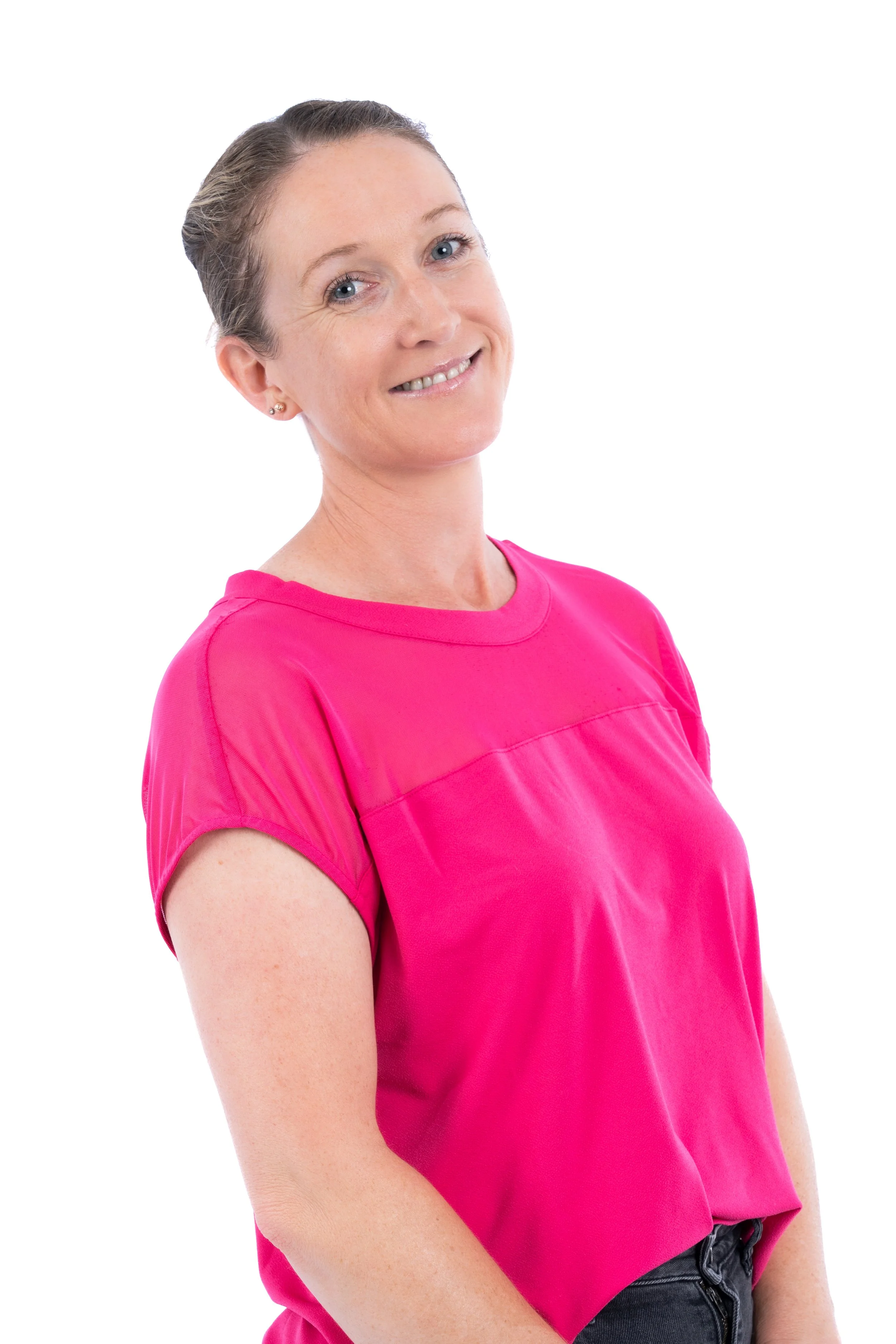 A woman with light skin and light brown hair tied back, wearing a bright pink t-shirt, smiling against a plain white background.