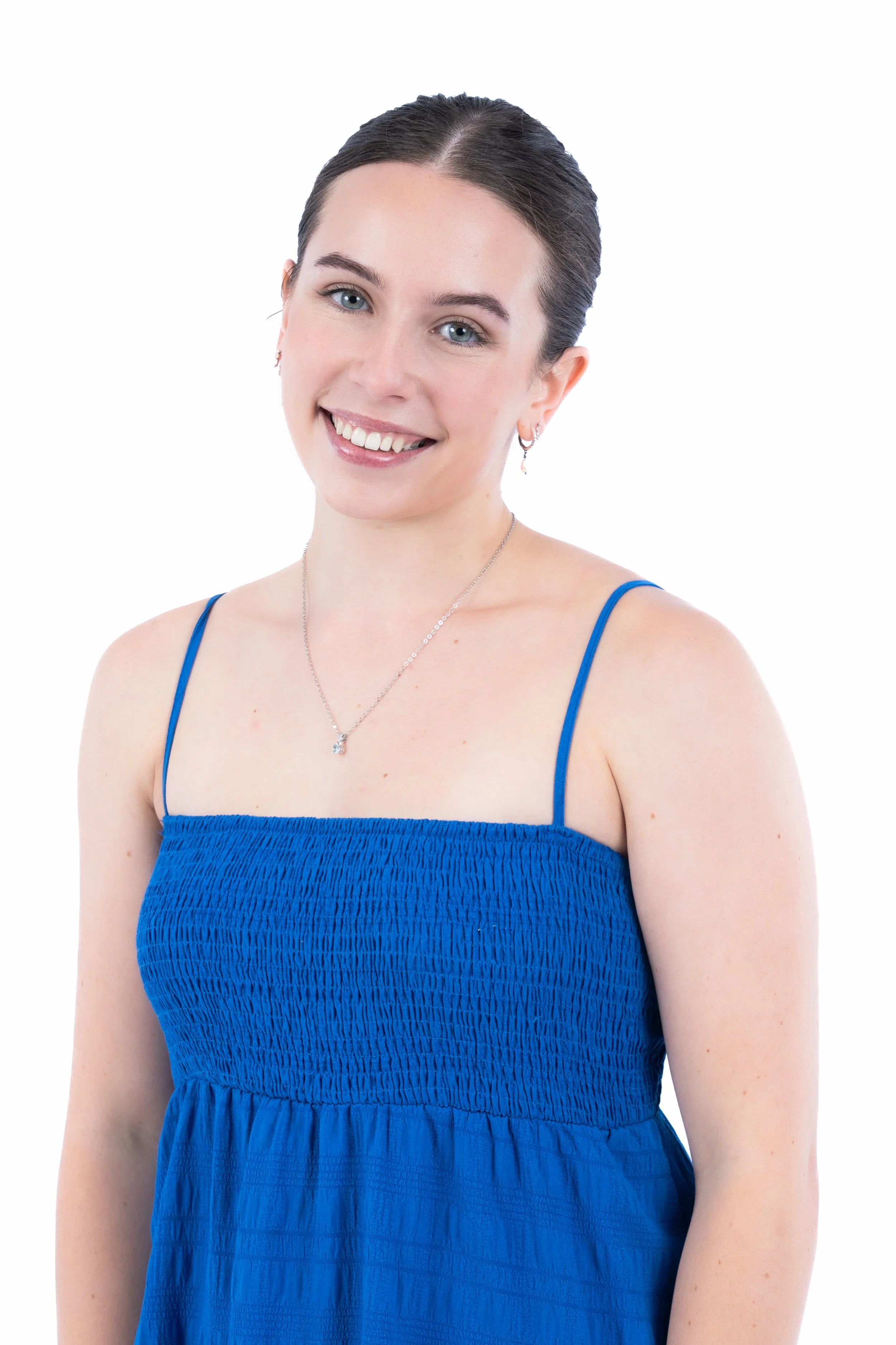 A young woman with dark hair pulled back, wearing a blue sleeveless dress and jewelry, smiling at the camera against a plain white background.