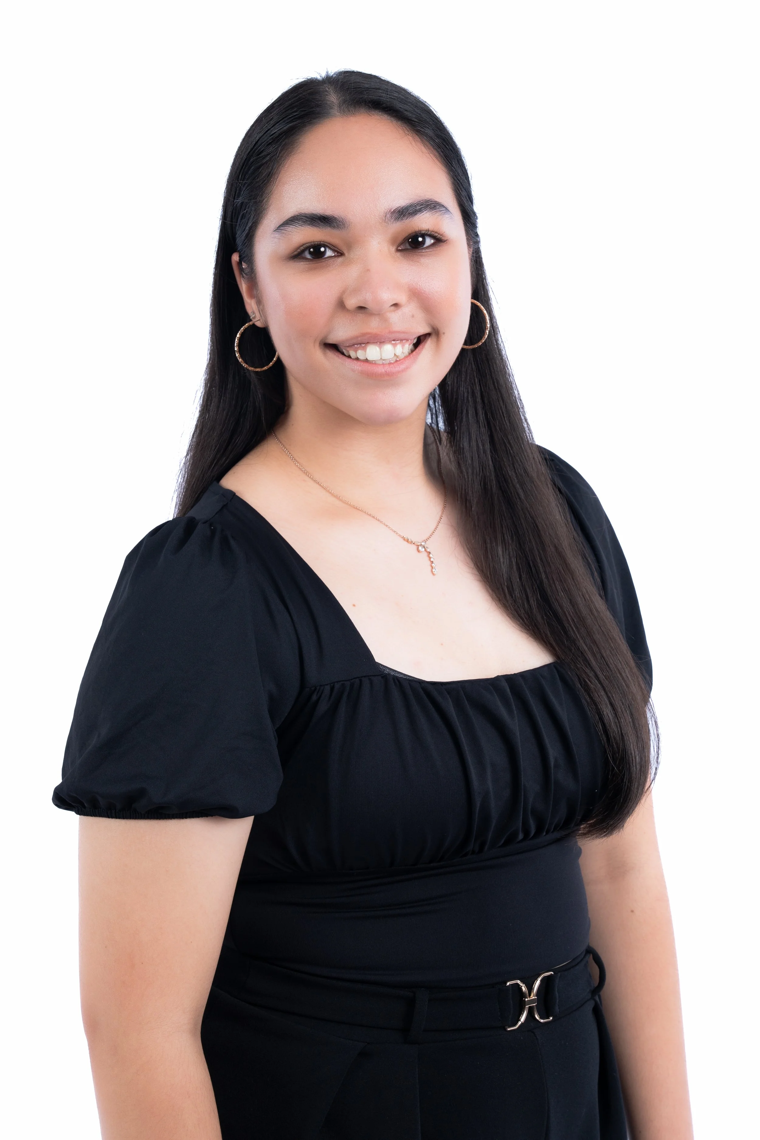 A young woman with long dark hair, wearing a black dress and gold jewelry, smiling at the camera on a white background.