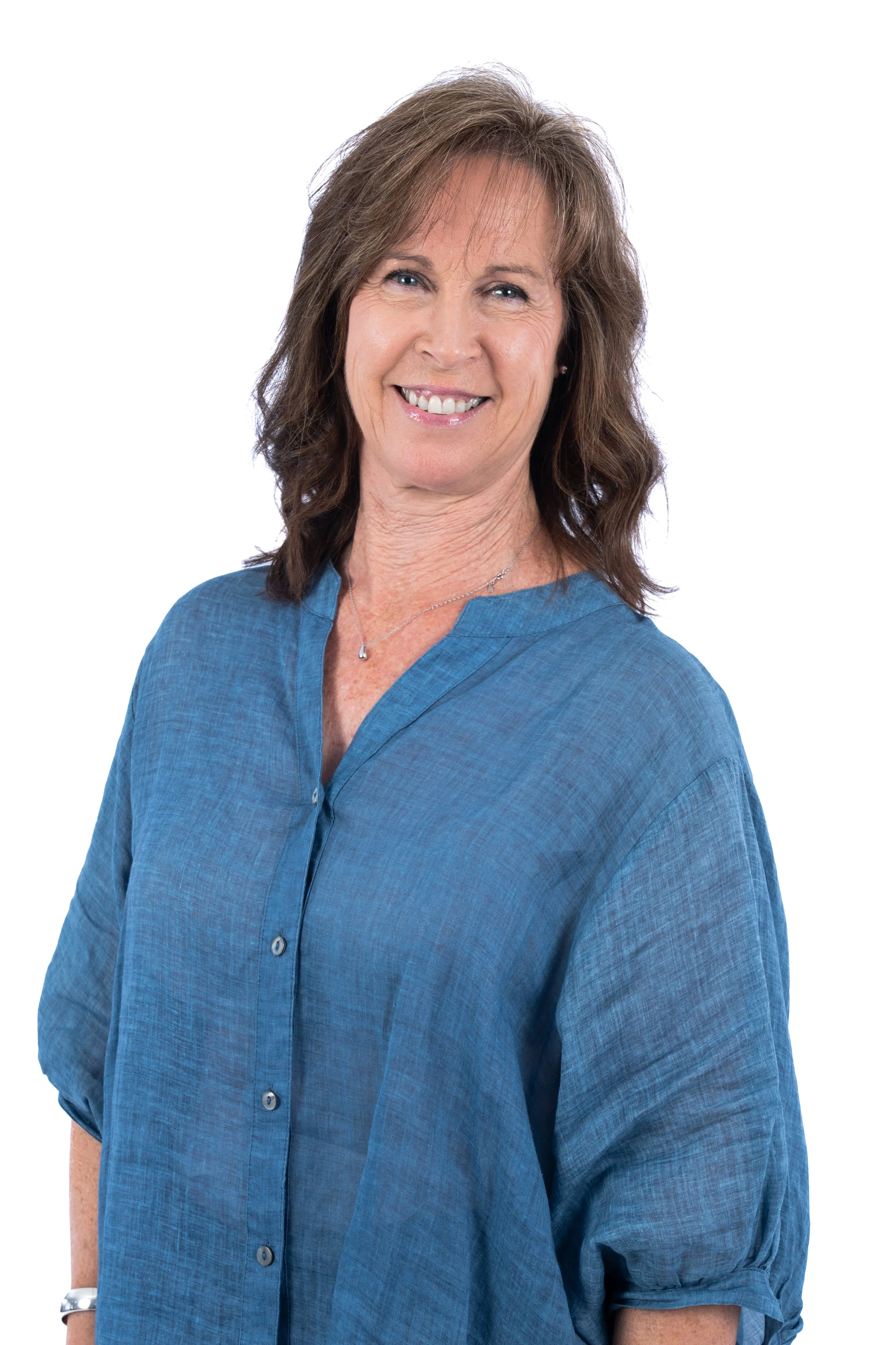 A woman with shoulder-length brown hair smiling, wearing a blue button-up shirt, against a white background.