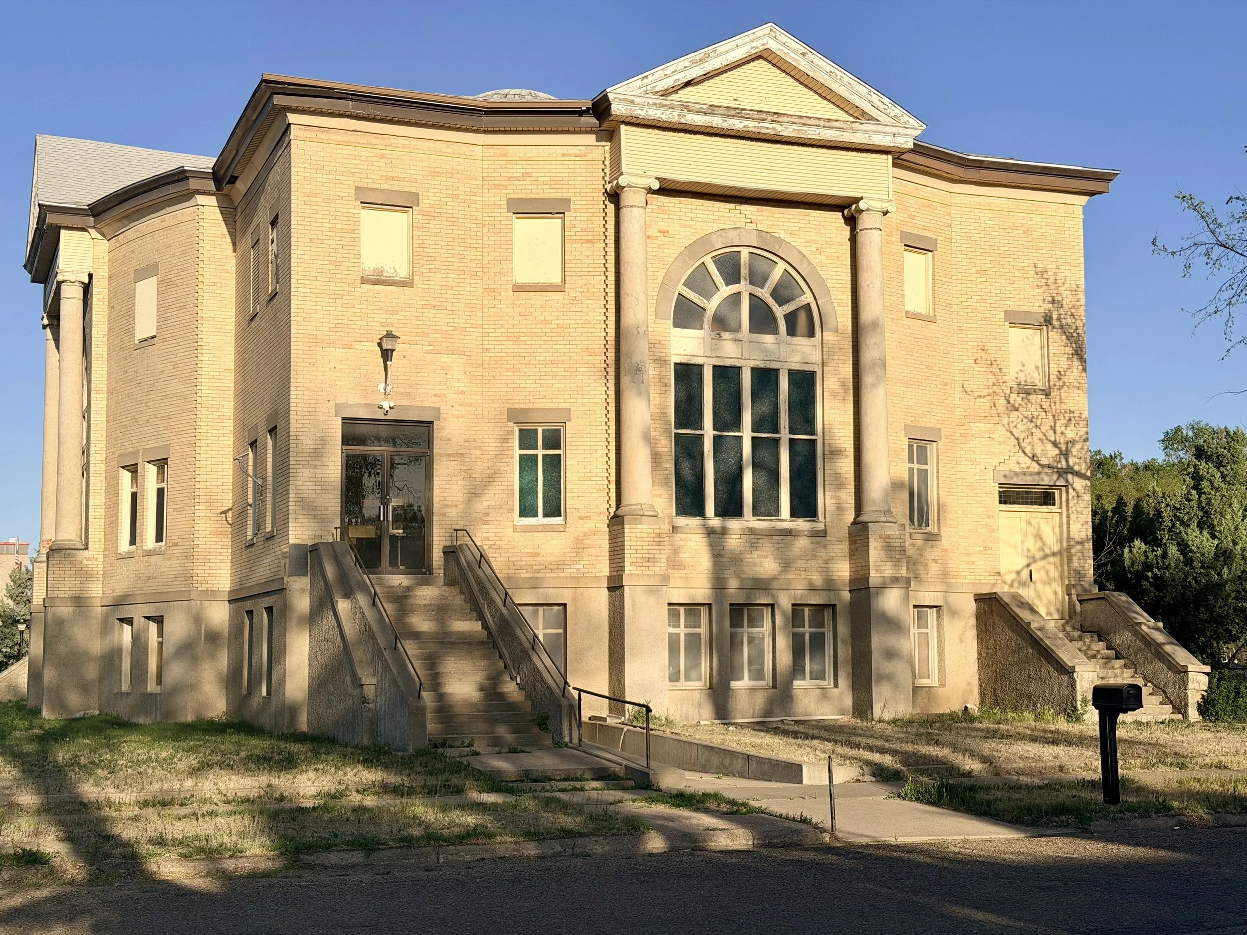 A historic building with brick walls, large arched windows, columns, and set of stairs leading up to the entrance, under a clear blue sky.