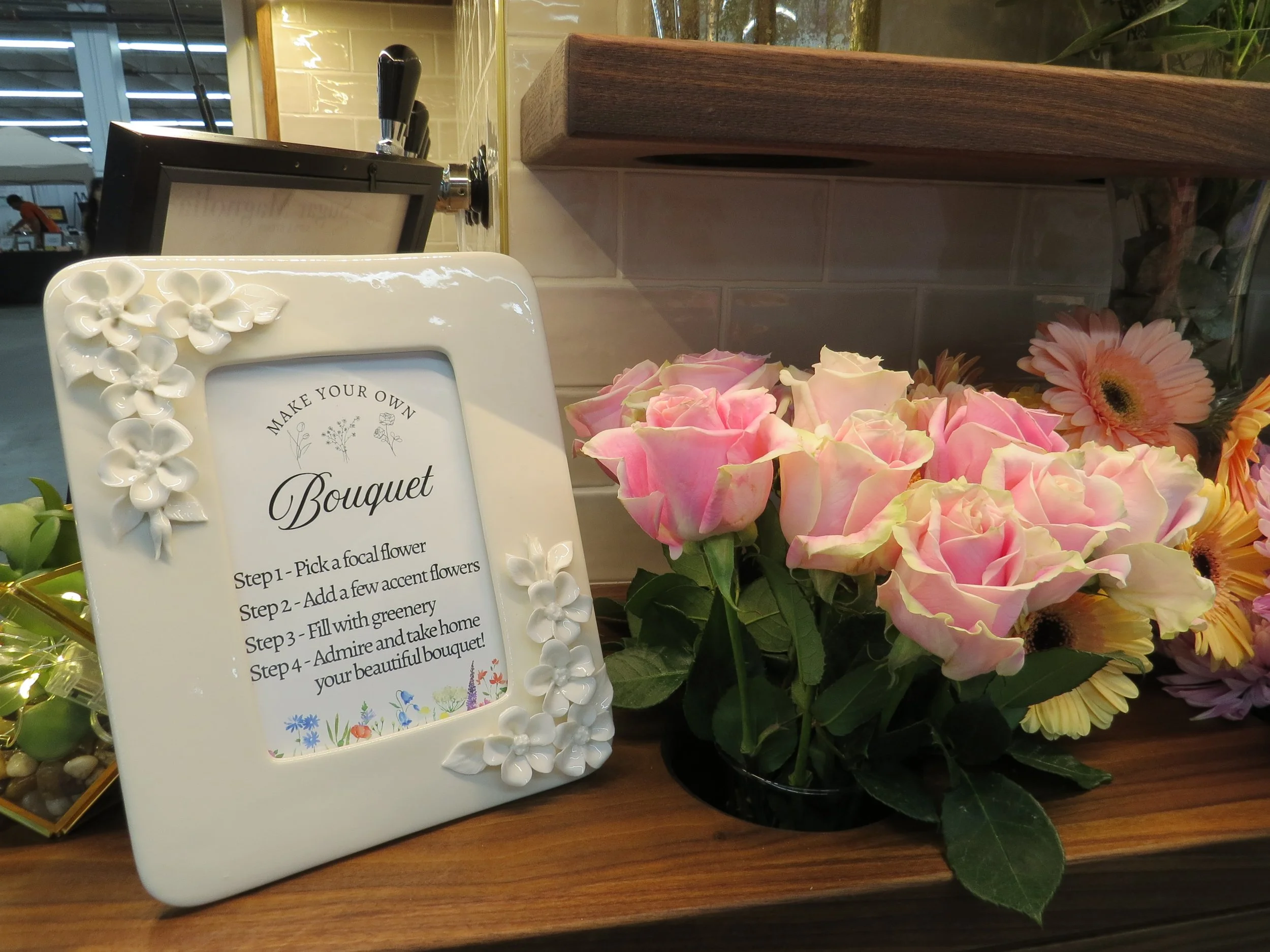 Array of flower arrangements in white vases displayed on glass shelves against a hexagonal tiled wall.
