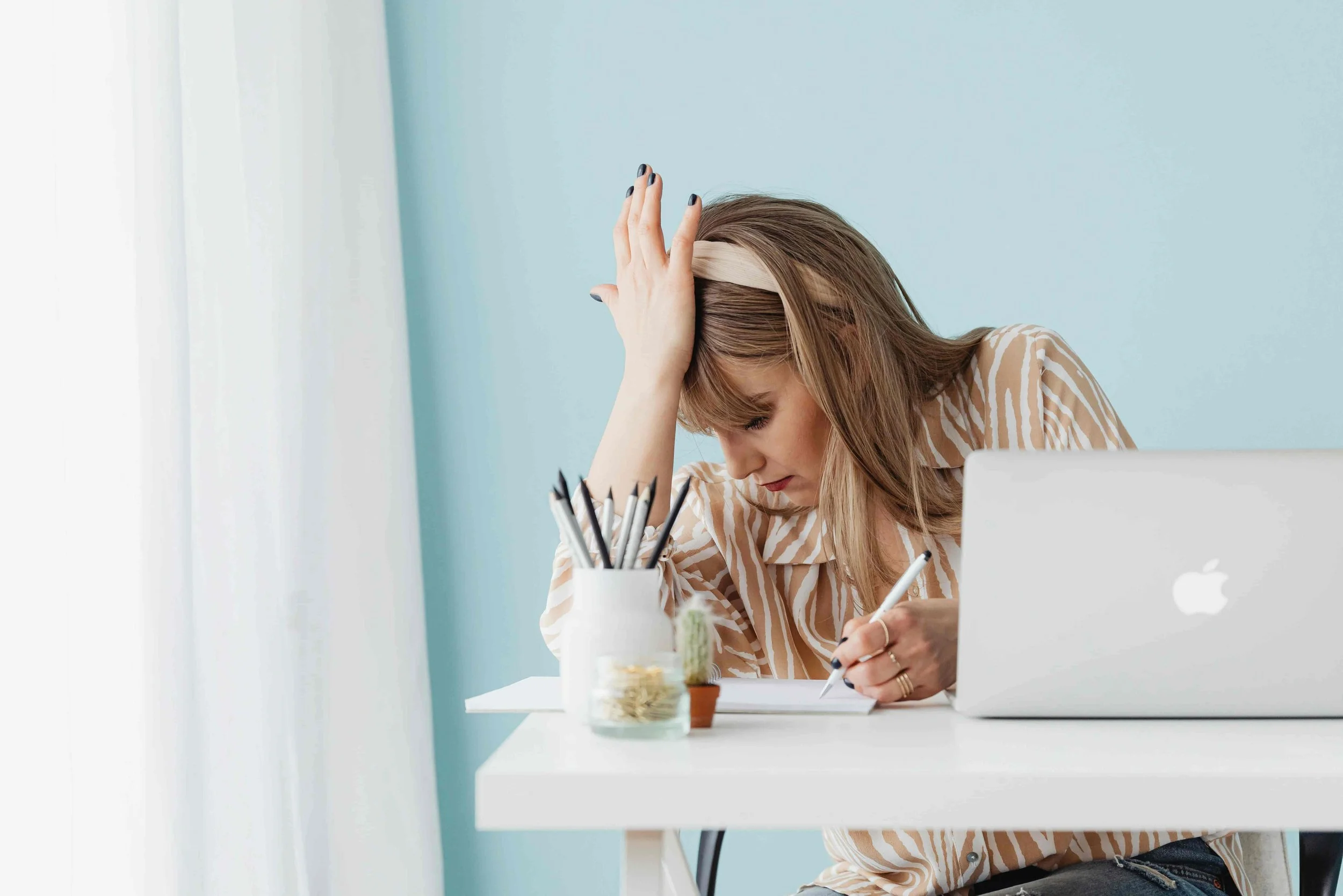 Woman with hand pressed against her forehead, she appears to be stressed or in deep thought. Image has a blockstyle-border
