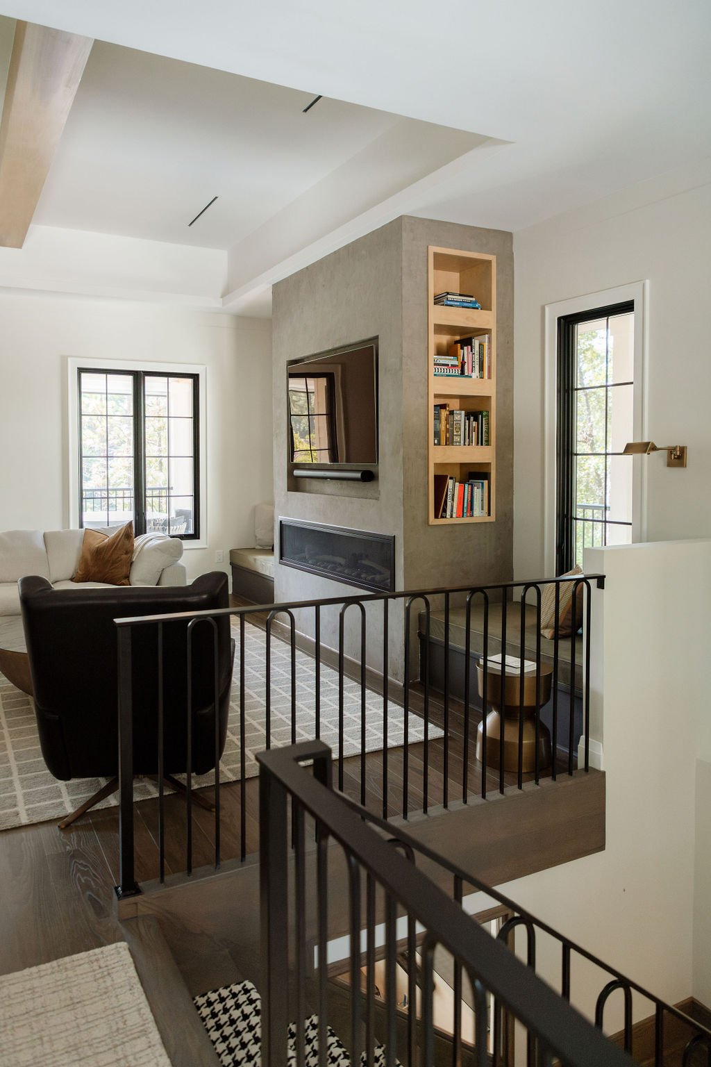Modern living room with concrete fireplace, built-in shelving, and layered seating by Batten Court Design.