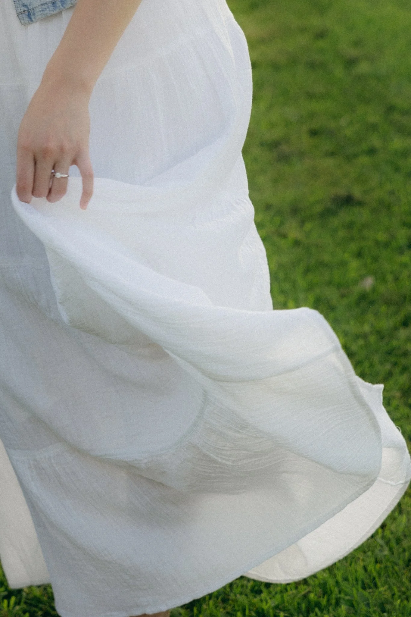 Close-up of a person holding a flowing white skirt or dress outdoors on green grass.
