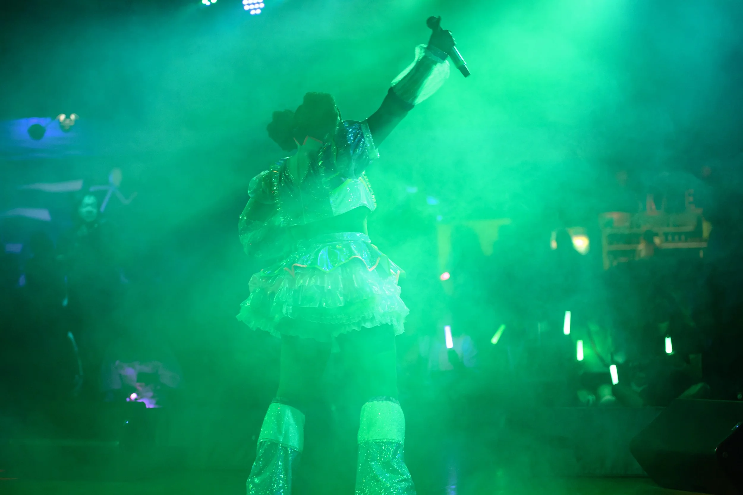 Person in colorful costume performing on stage, with green lighting and a smoky atmosphere.