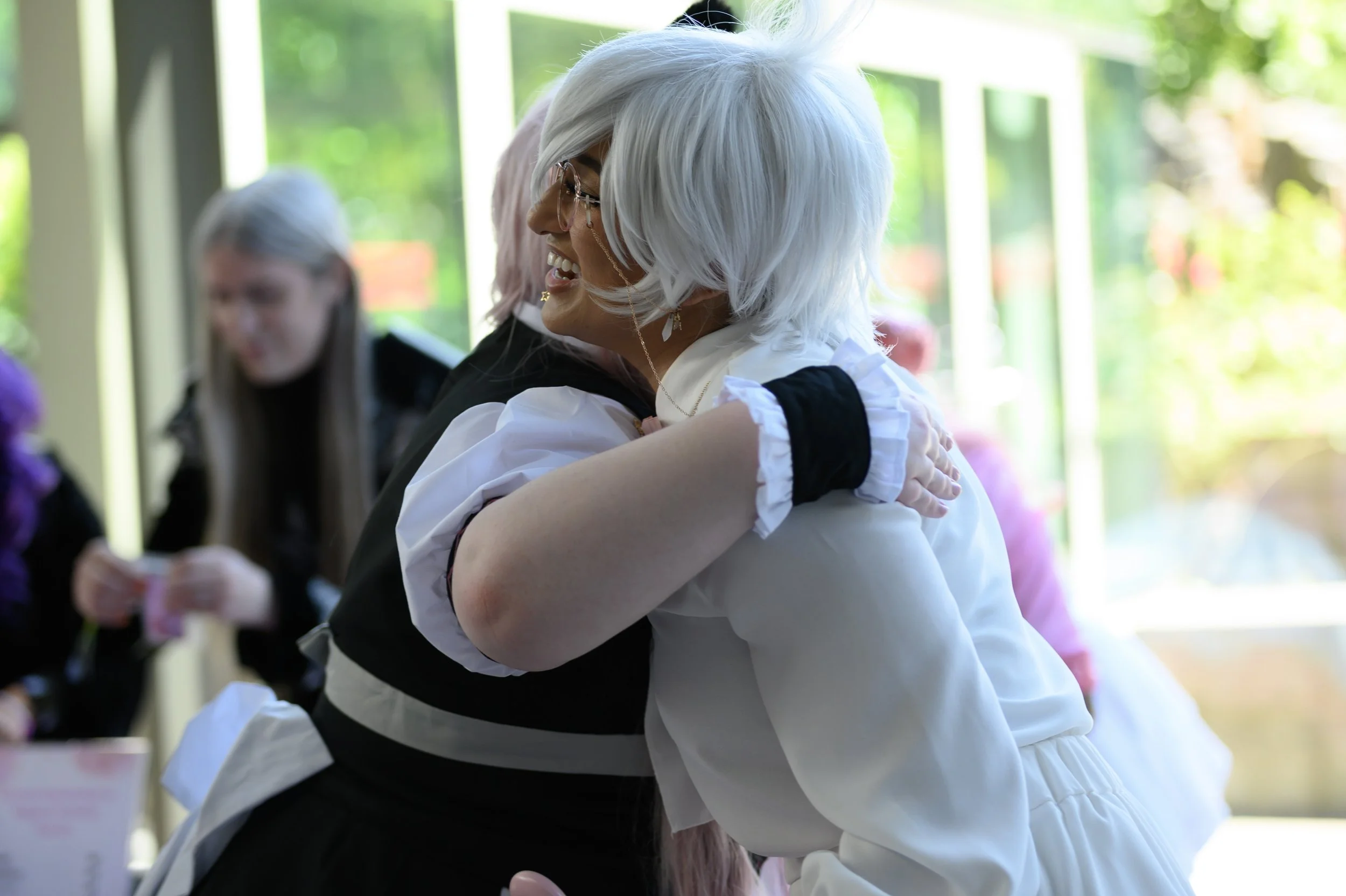Two women, on with white hair embrace each other and smile warmly in a bright indoor space.