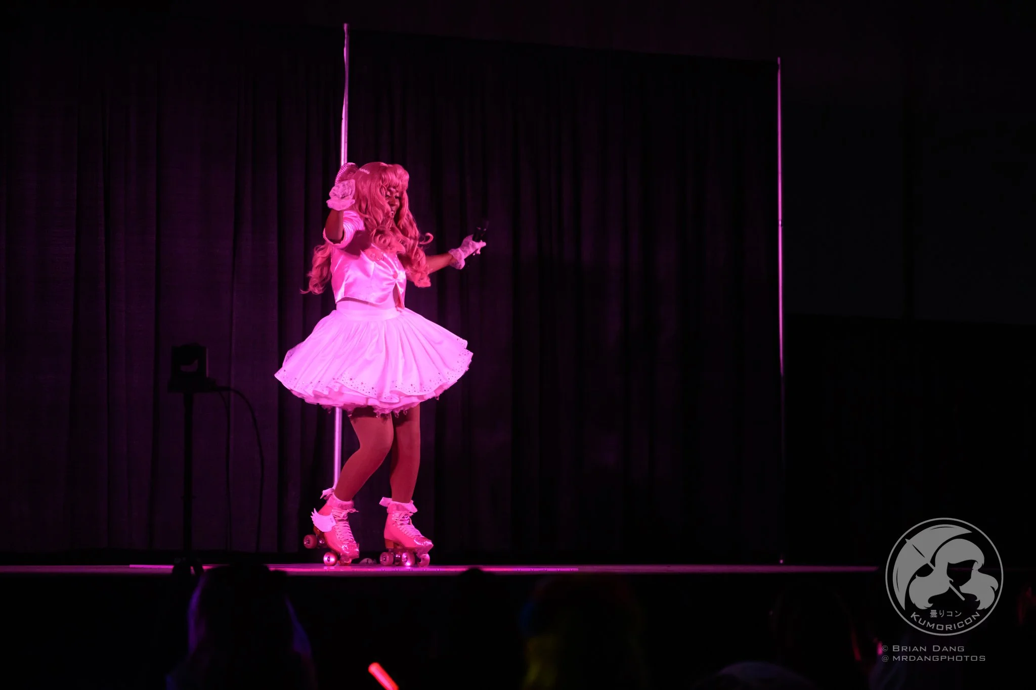 Performer dressed in pink roller skate costume on stage during a performance with black curtains in the background.