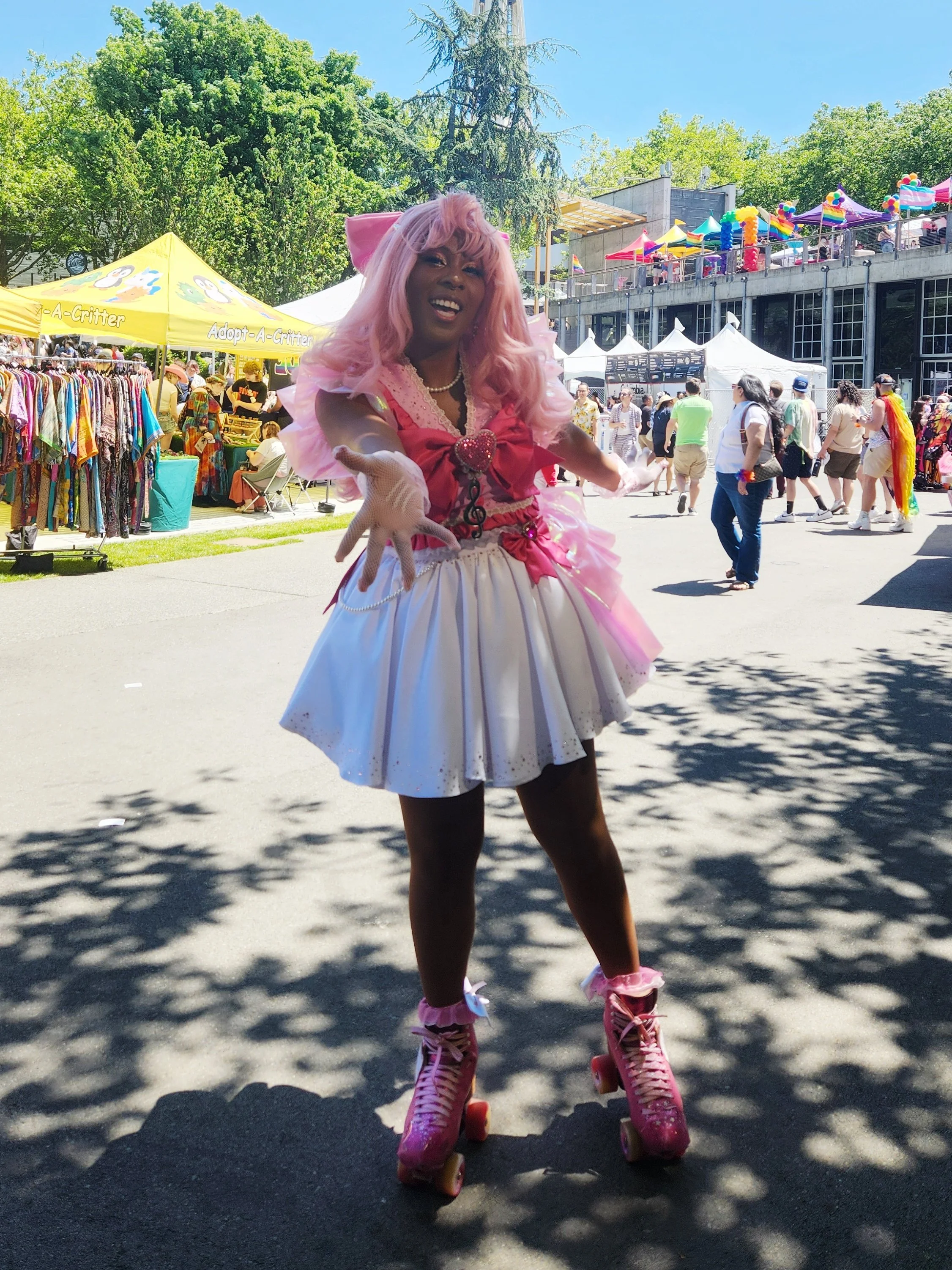 Person with pink hair dressed in pink and white outfit, wearing pink roller skates, at an outdoor festival with tents and trees