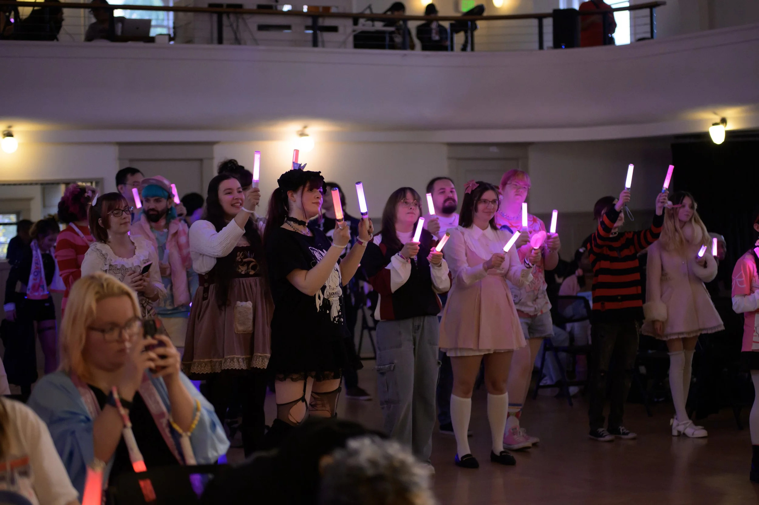 Group of people at a concert or event holding colorful glow sticks, standing and watching attentively.