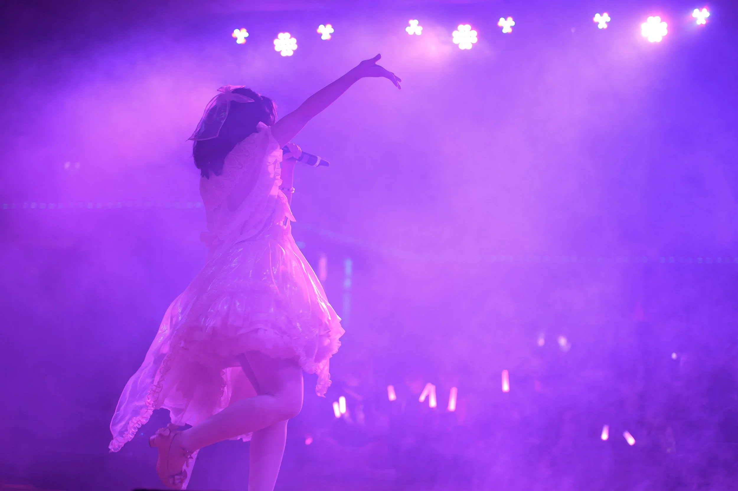 A girl in a pink dress holding a microphone on stage with purple lighting and fog effects.