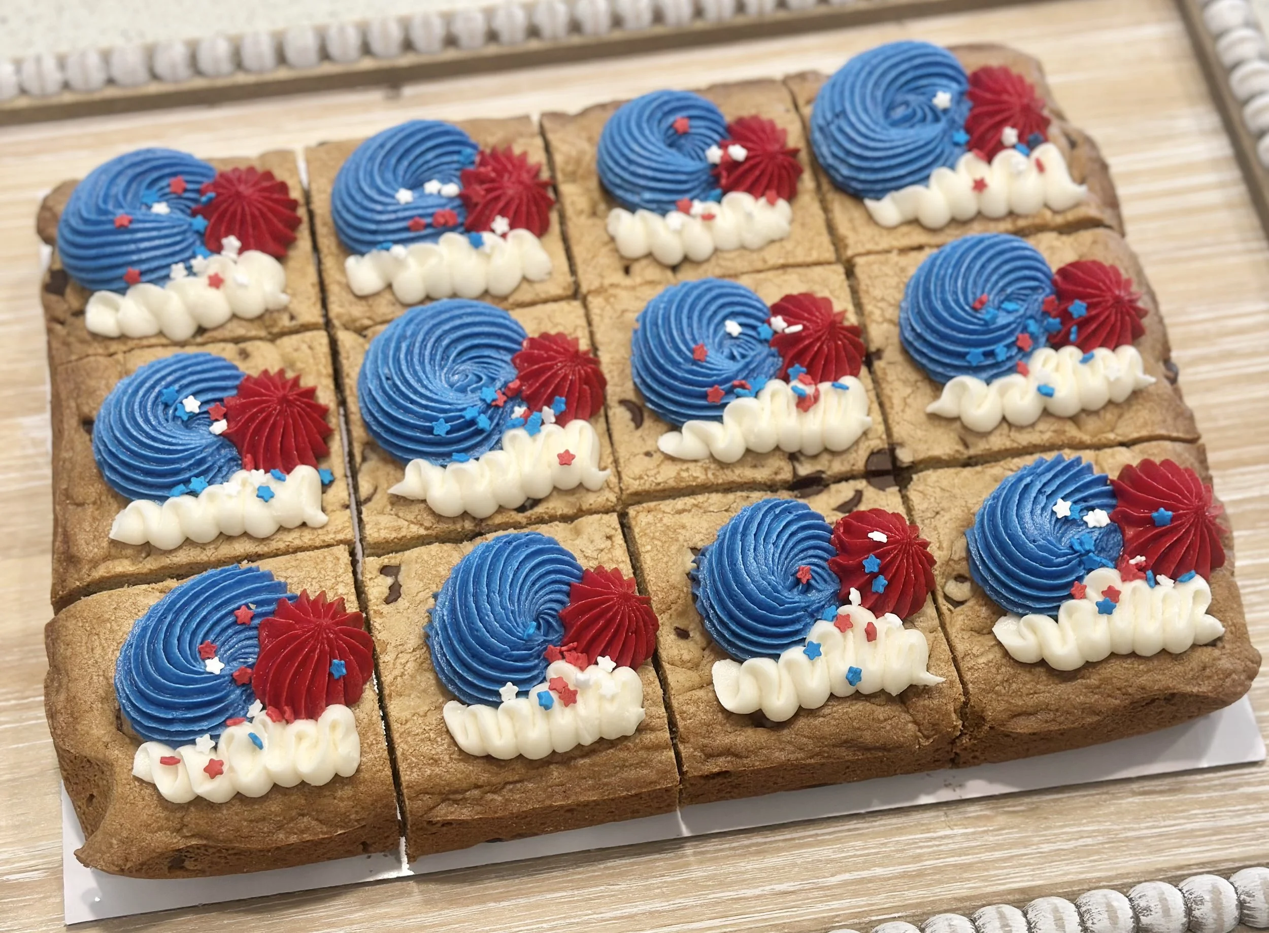 A tray of twelve decorated cookies with patriotic red, white, and blue cream frosting and sprinkles.