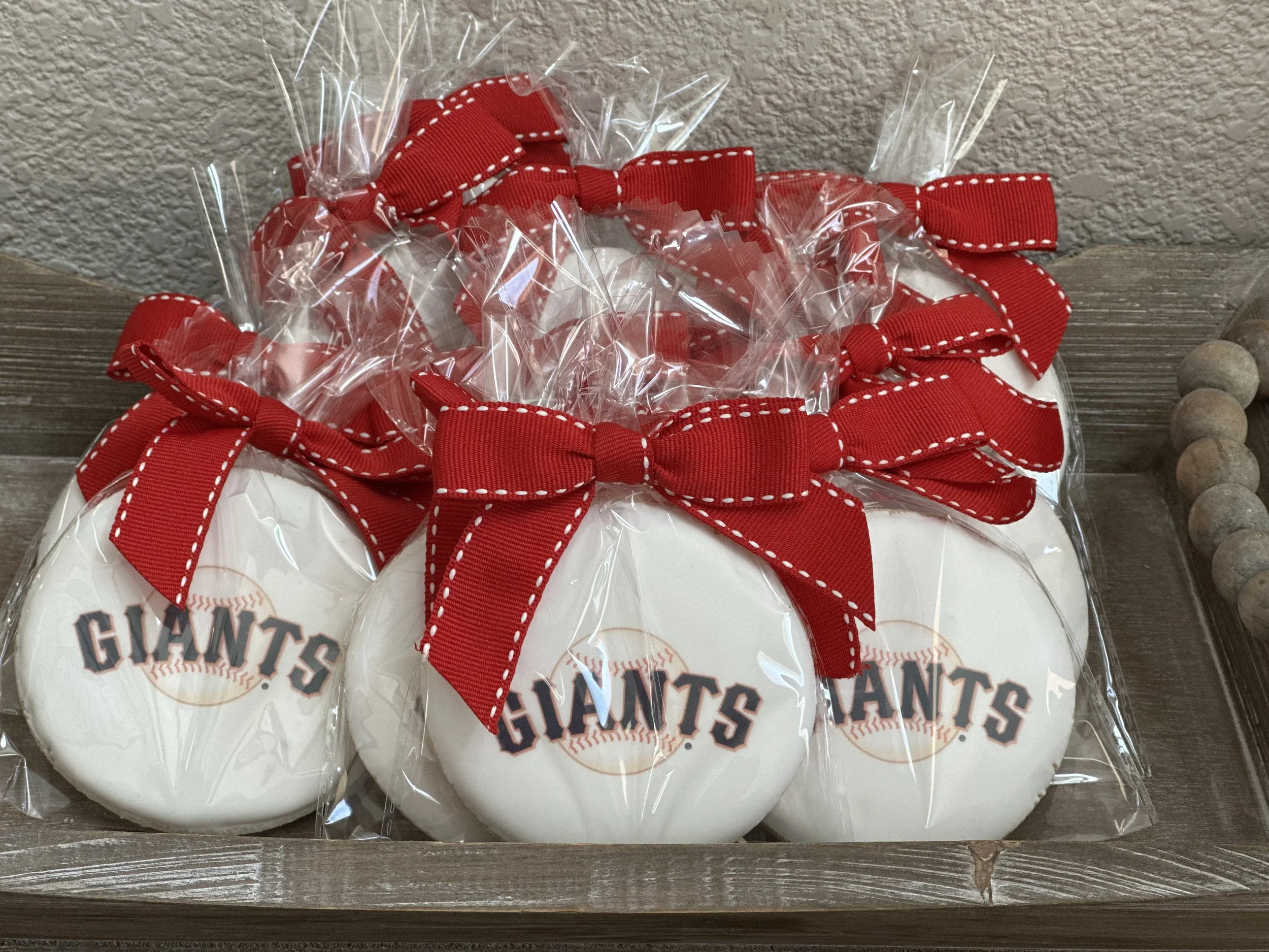 Sugar cookies decorated with the San Francisco Giants logo, wrapped in clear plastic and tied with red bows.