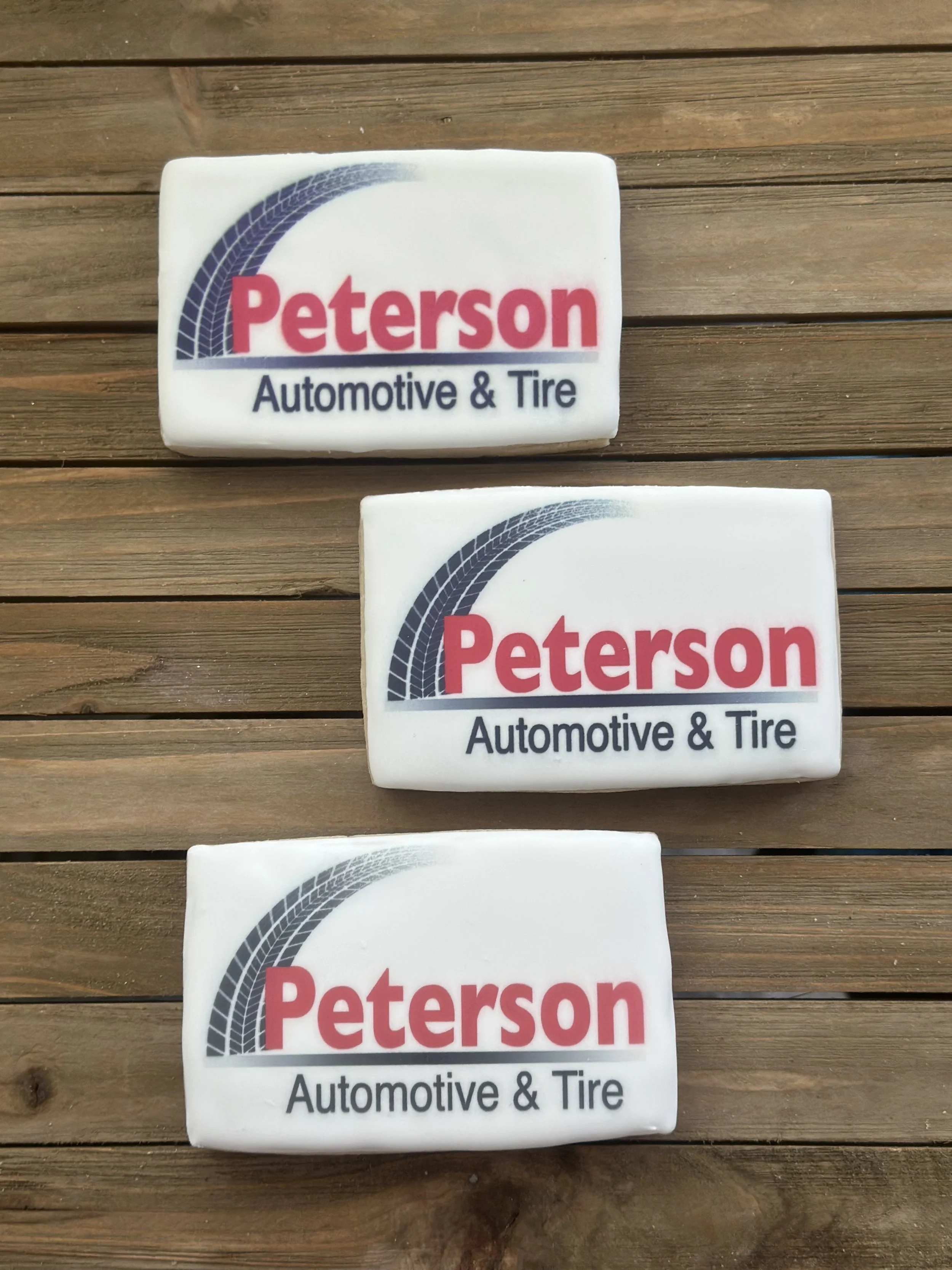 Three white Bars of soap with a logo and text for 'Peterson Automotive & Tire' placed on a wooden surface. The logo features a curved tire track design.
