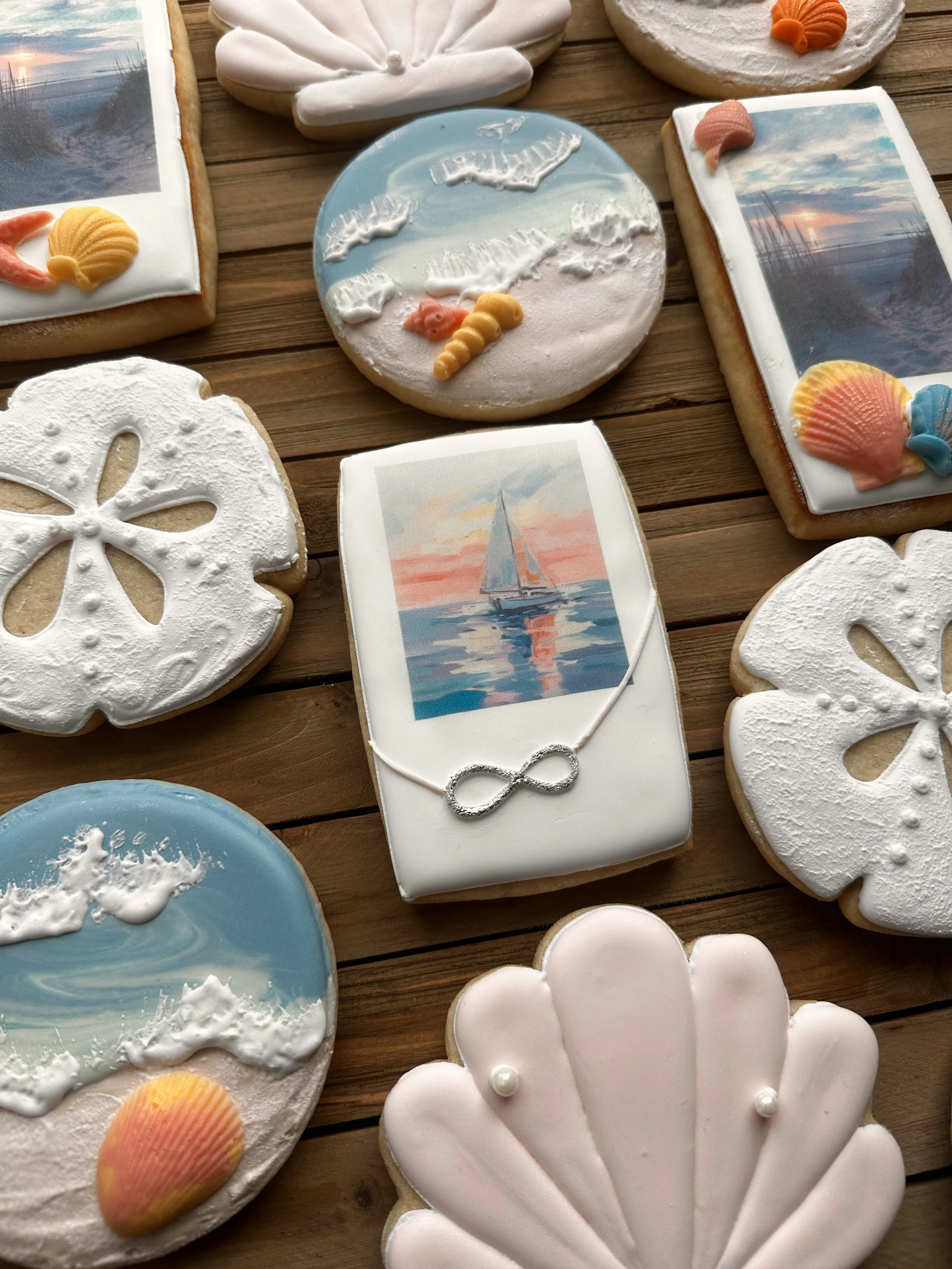 Decorative cookies with coastal and sailing themes, including images of seashells, seagulls, sailboats, and ocean scenes, arranged on a wooden surface.