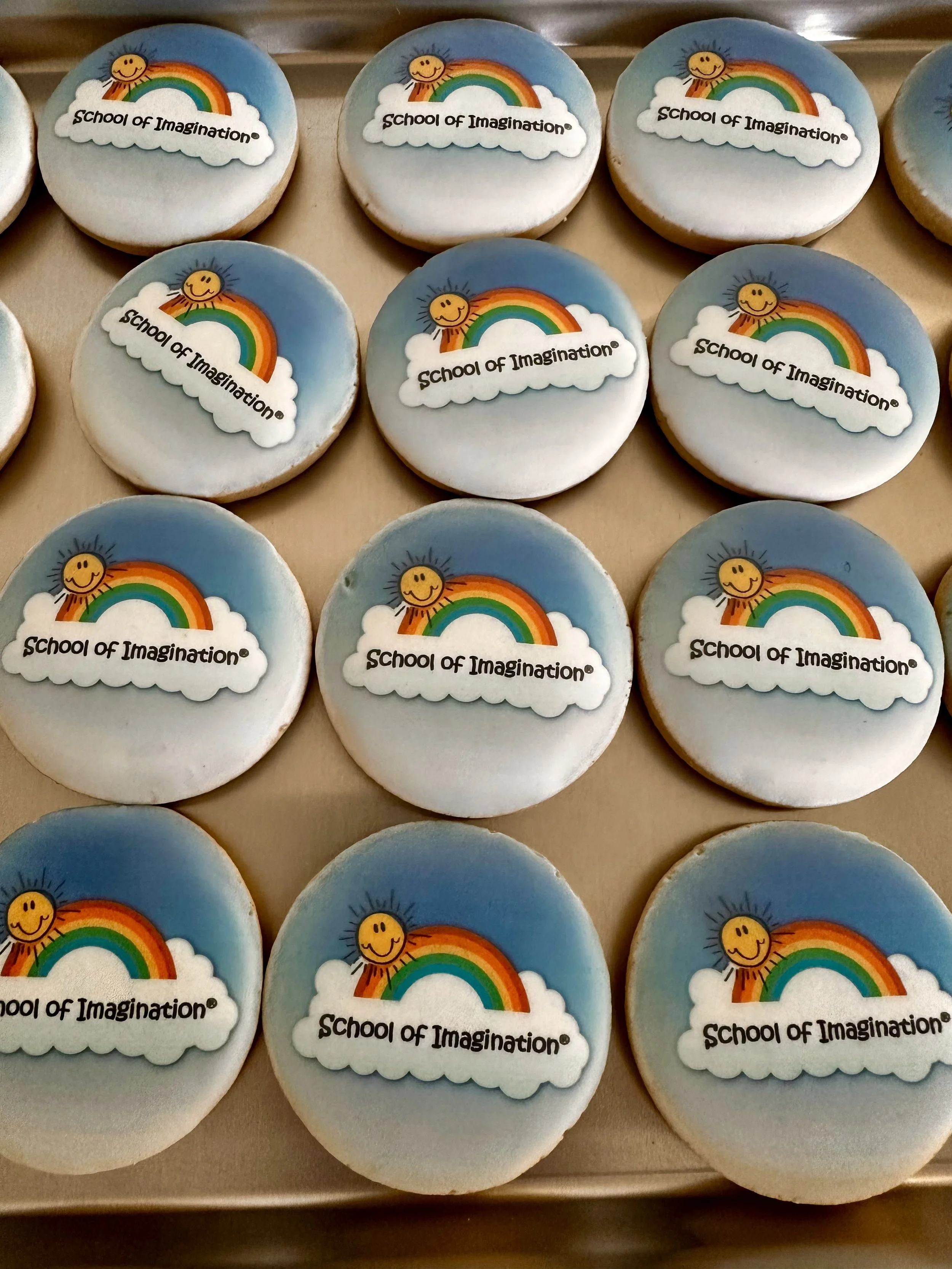 Decorated cookies with a rainbow and smiling sun, displaying the text 'School of Imagination.'
