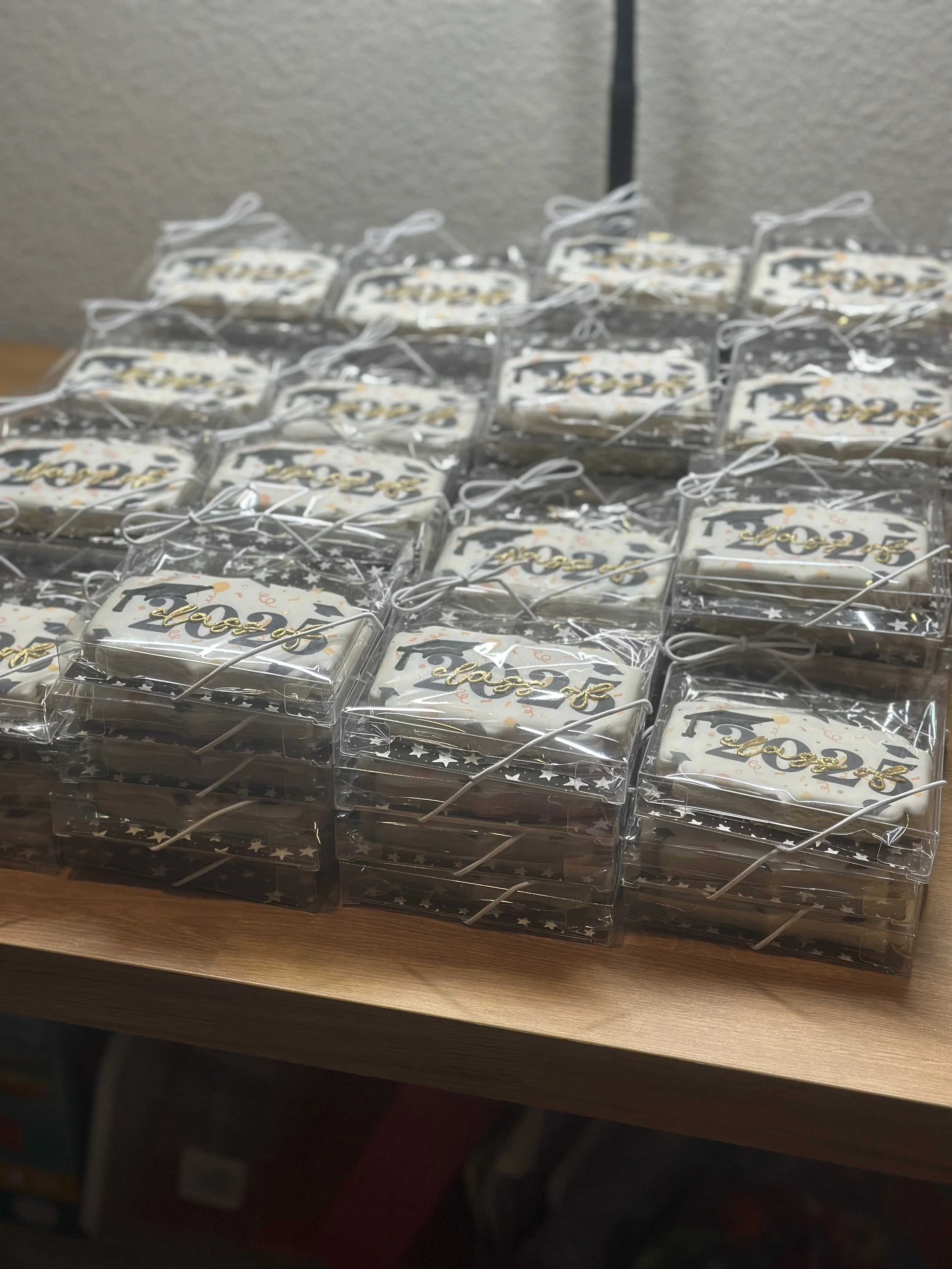 Multiple small decorated cookies individually wrapped in clear plastic with white ribbons, arranged on a table, celebrating a New Year's event for 2023.