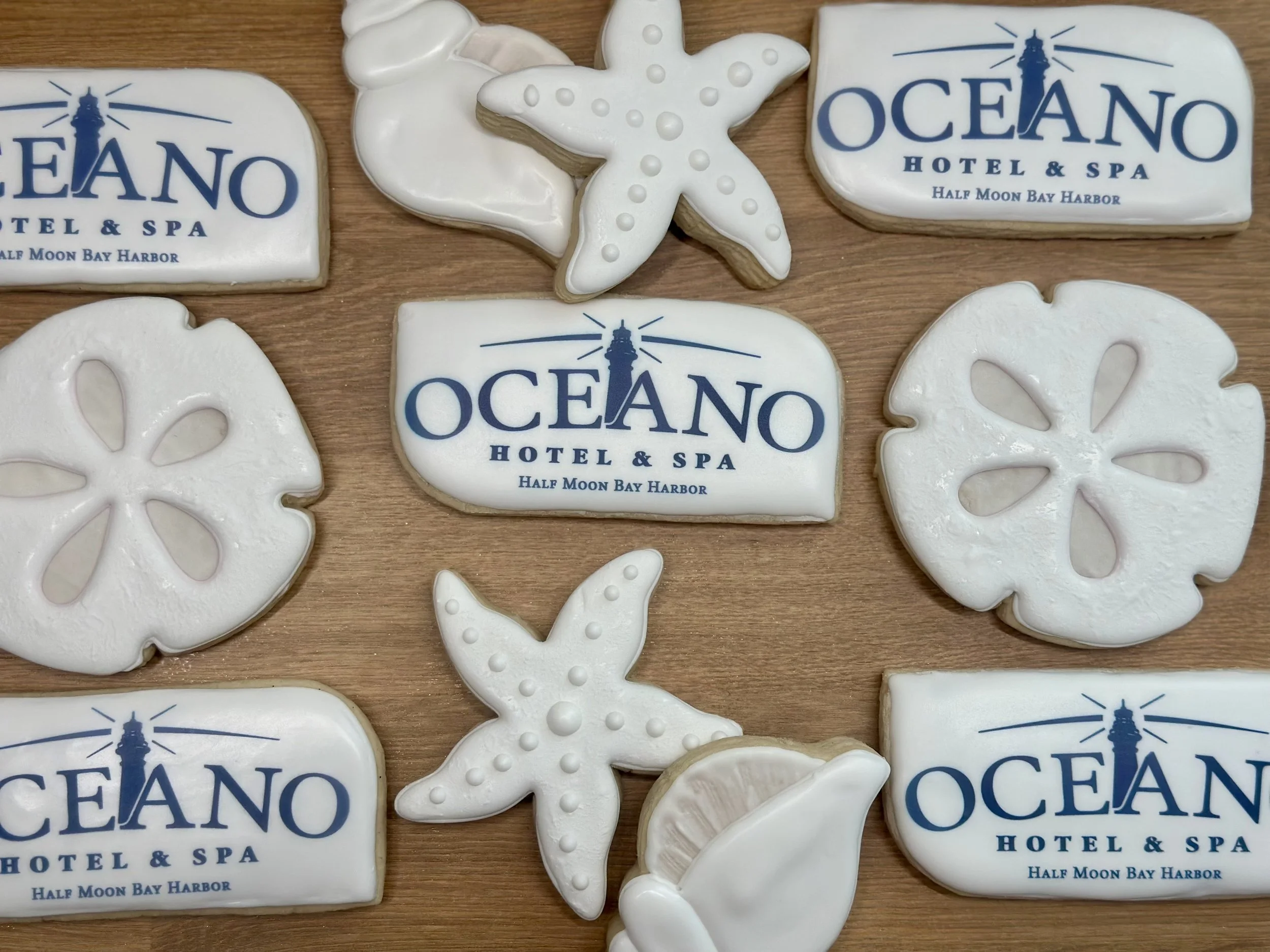 Decorative cookies with Oceano Hotel & Spa logo, starfish, sand dollar, and lemon wedges designs on a wooden surface.