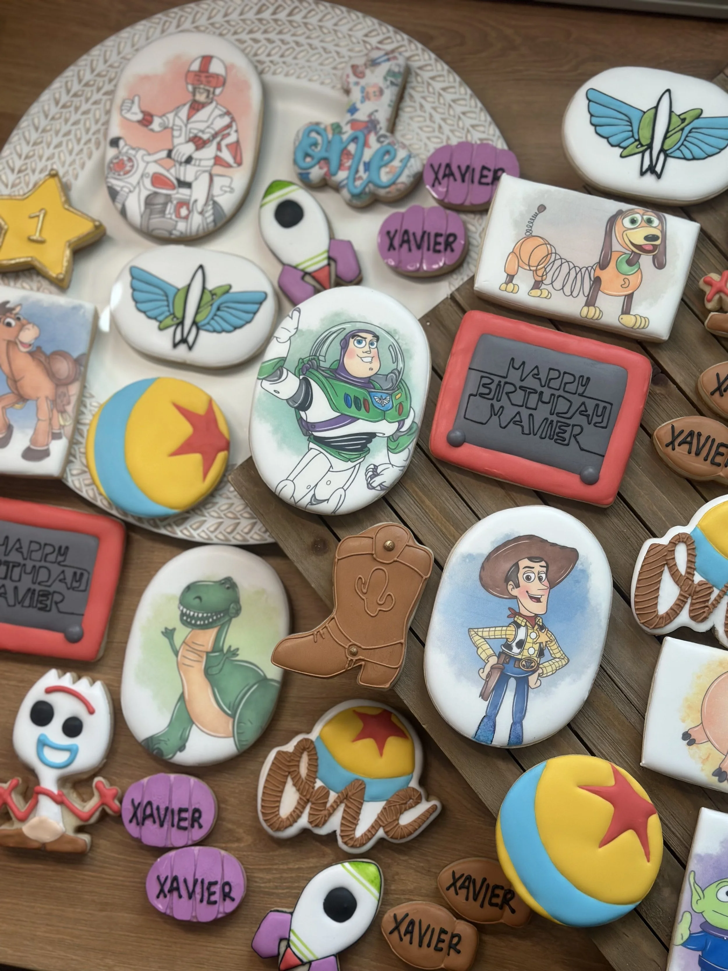Collection of decorated cookies featuring characters from Toy Story, Buzz Lightyear, Woody, Rex, and Bo Peep, along with birthday themed cookies, balloons, and the name 'Xavier' written on some cookies.