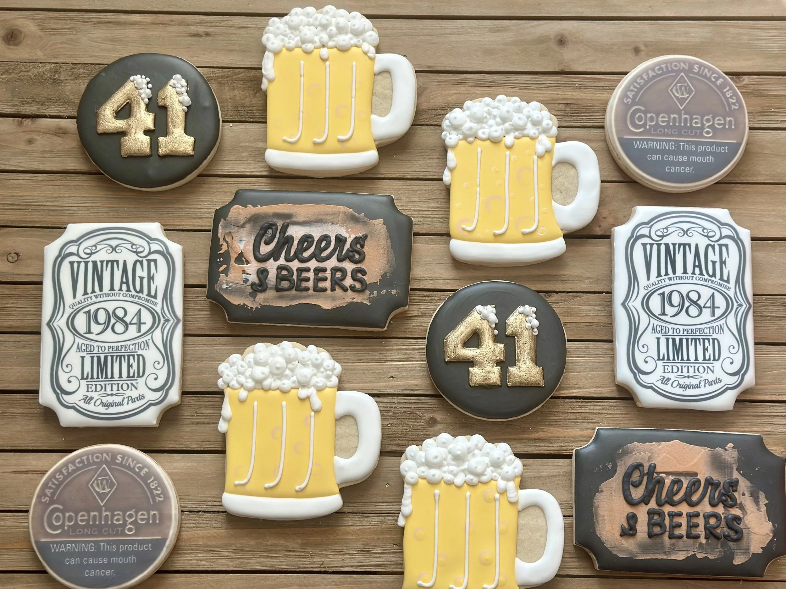 Collection of decorated cookies on a wooden surface, including mugs of beer, birthday number 41, vintage labels, and beer brand cookies.