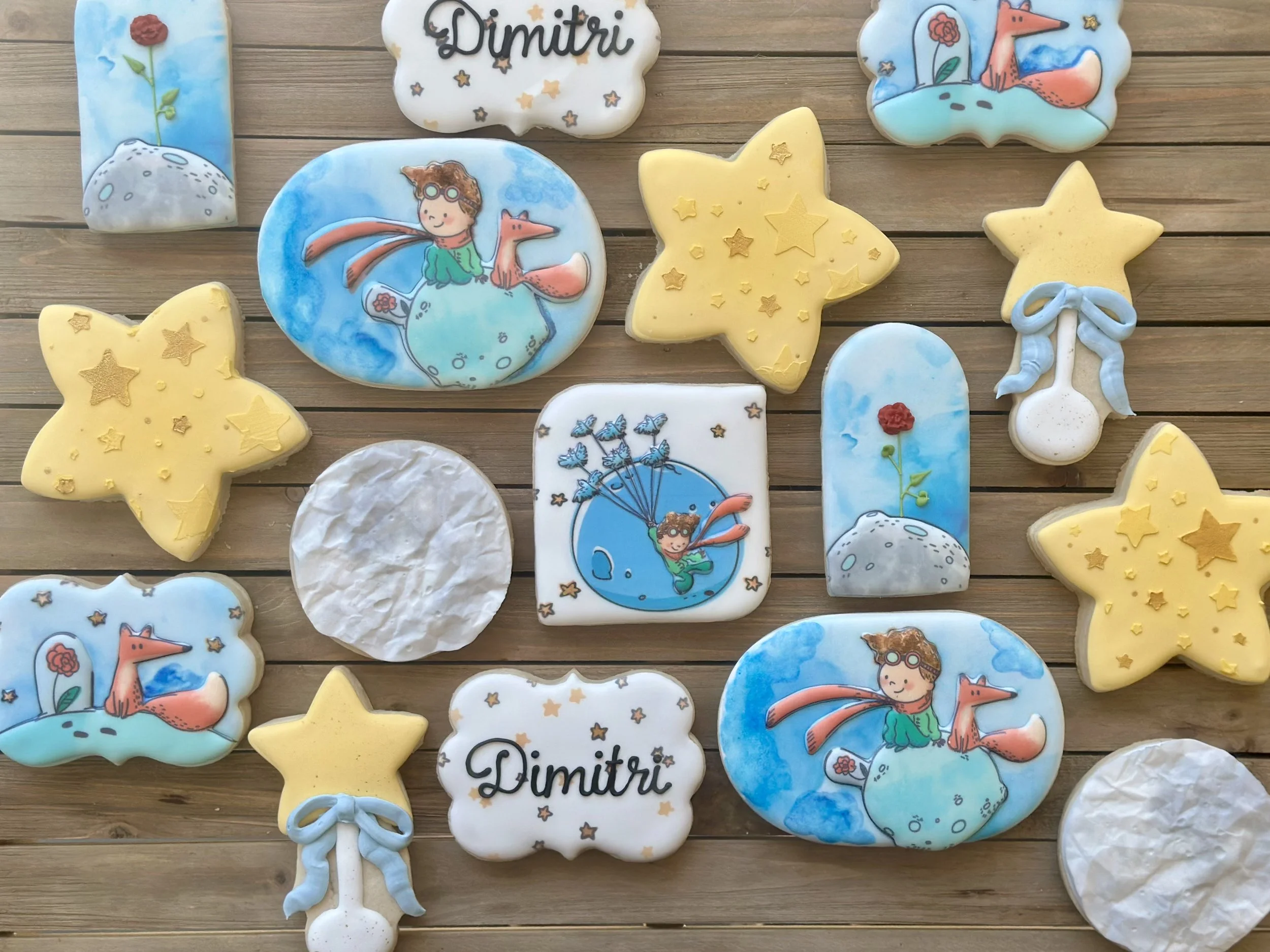 Decorative cookies themed with stars, clouds, a moon, and Boy with Fox illustration, some with the name 'Dimitri', arranged on a wooden surface.