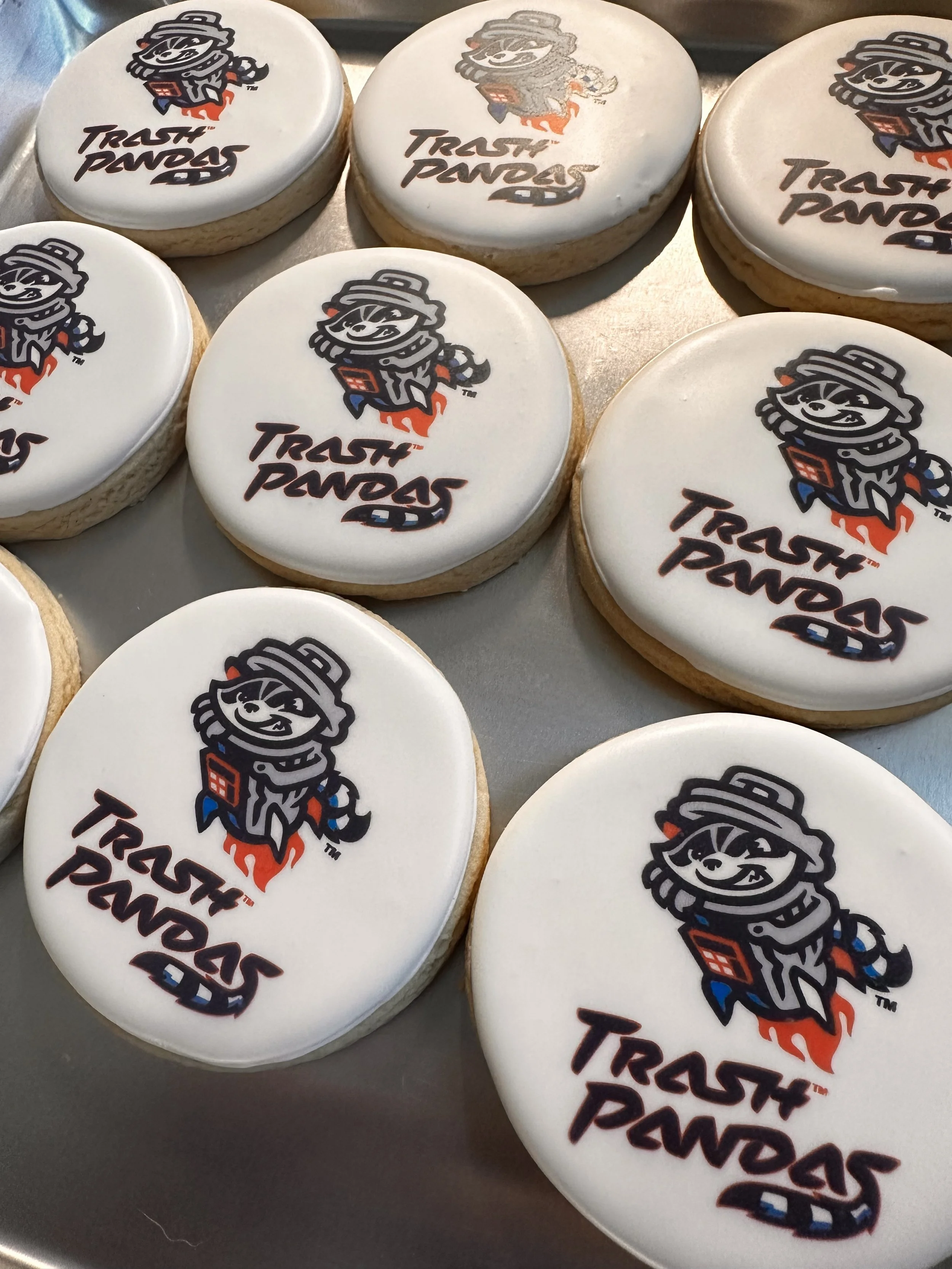 Several round cookies with white icing featuring a cartoon raccoon mascot and the words "Trash Pandas" on top.