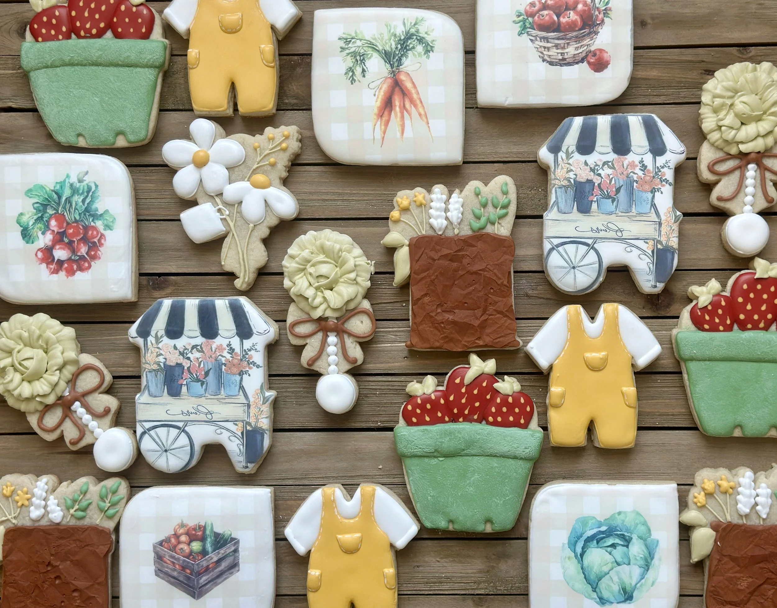 Decorative cookies with garden and fruit motifs arranged on a wooden surface, including strawberries, carrots, flowers, and garden carts.