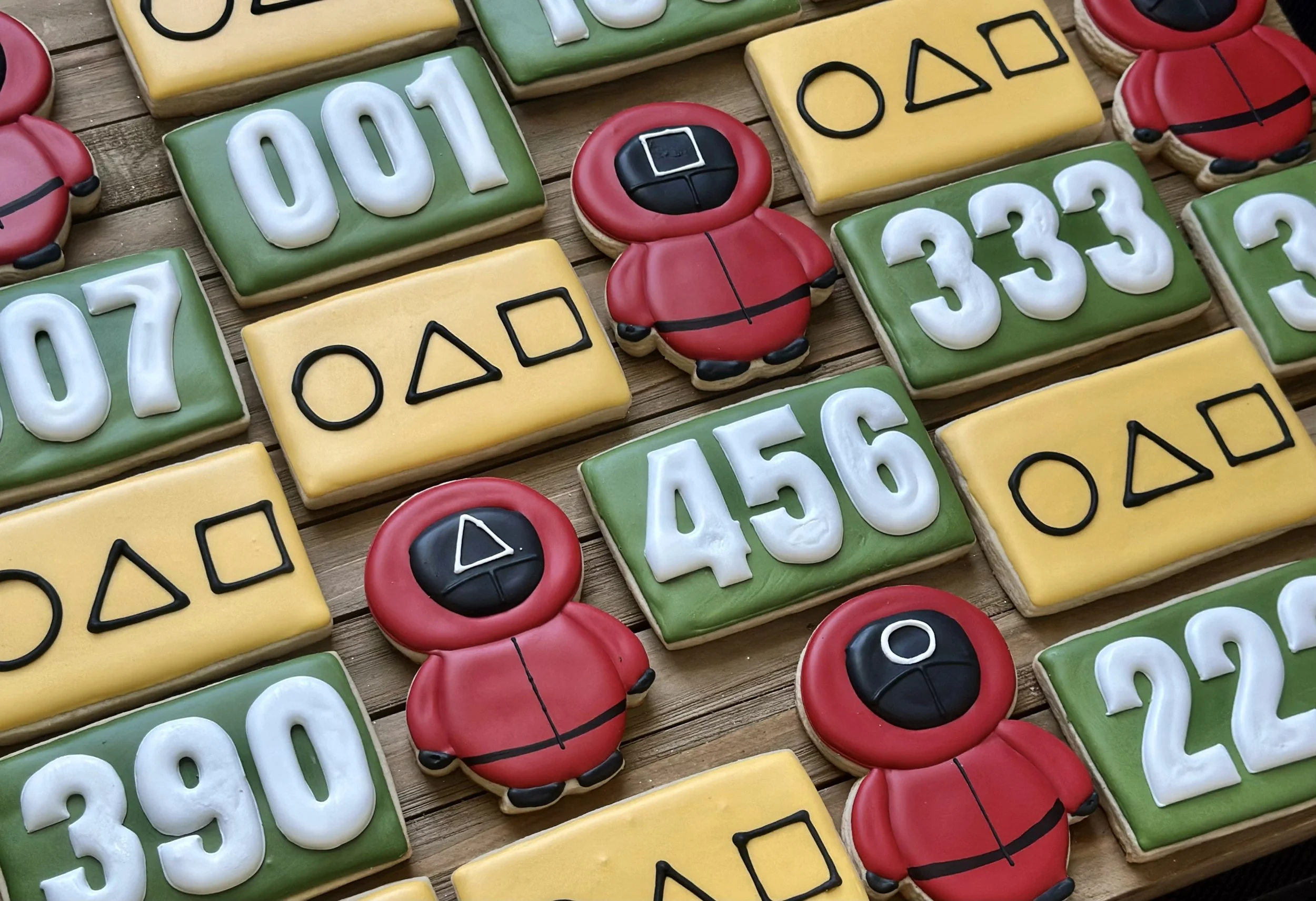 Decorated cookies shaped like game pieces from the PlayStation game, including numbered tiles, controller icons, and red character cookies on a wooden surface.