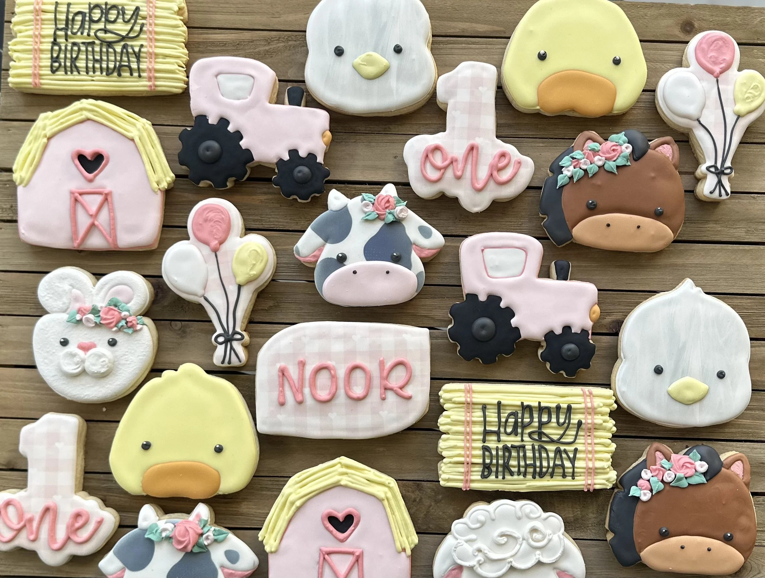 Assorted decorated cookies with farm animal and birthday themes on a wooden surface.