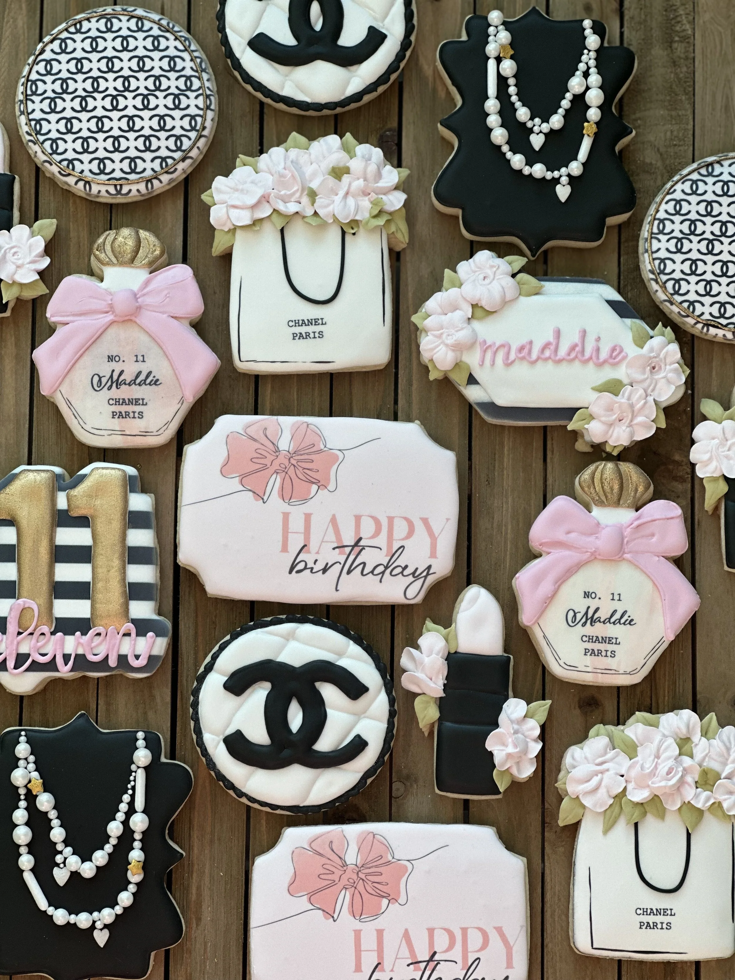 Decorative cookies with Chanel and makeup motifs, birthday greetings, and floral elements on a wooden surface.