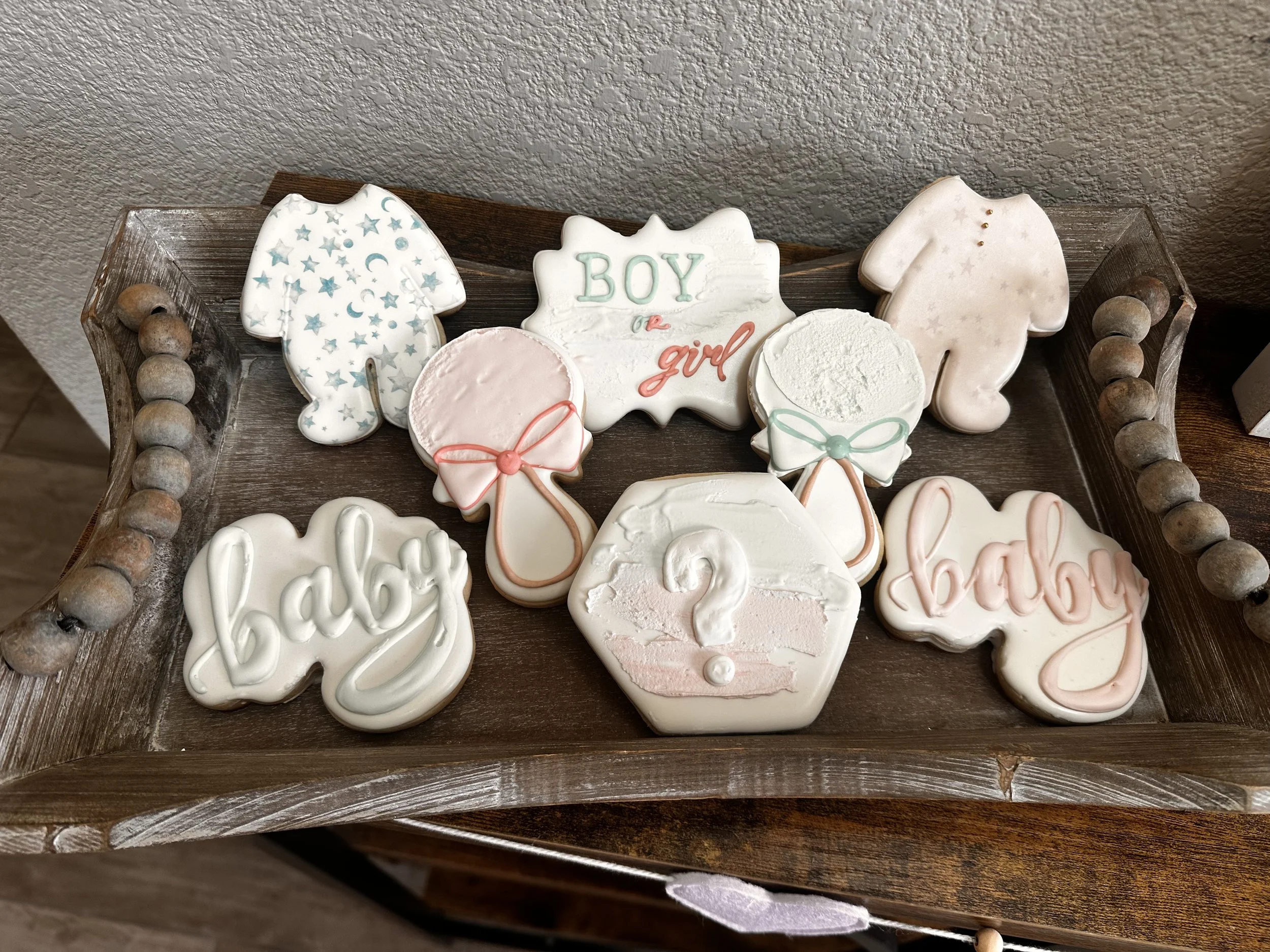 Baby shower cookies decorated with baby-themed designs, including ones with 'boy' and 'baby' written on them, a question mark, and pastel colors.